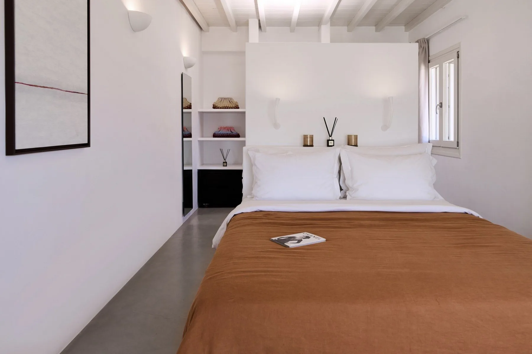 A bright bedroom with a bed dressed in white linens and a brown coverlet.