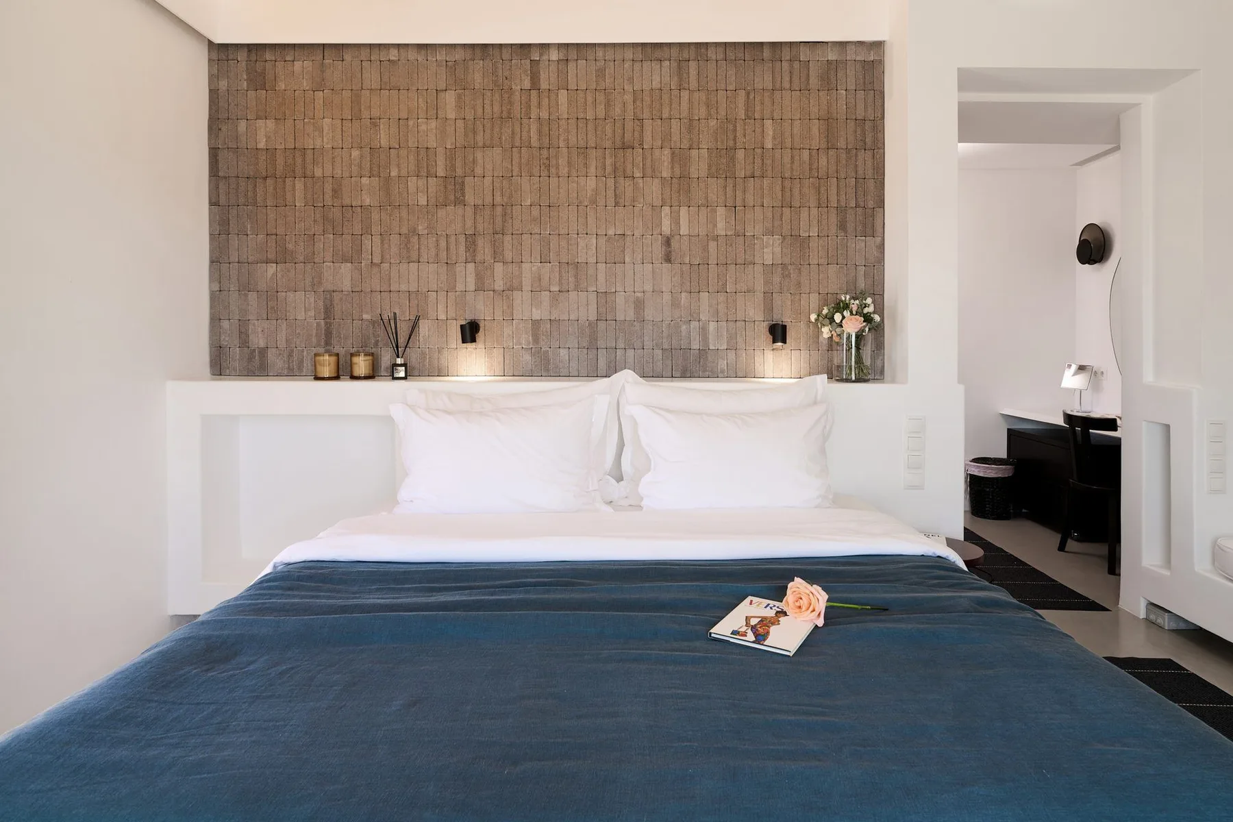 A bedroom with a neatly made bed and textured wall behind the headboard.