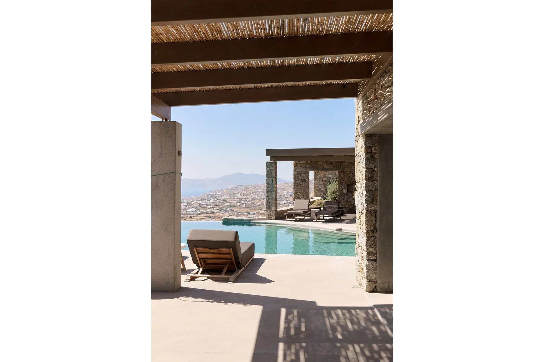 A swimming pool beside a shaded patio, with distant hills beyond.