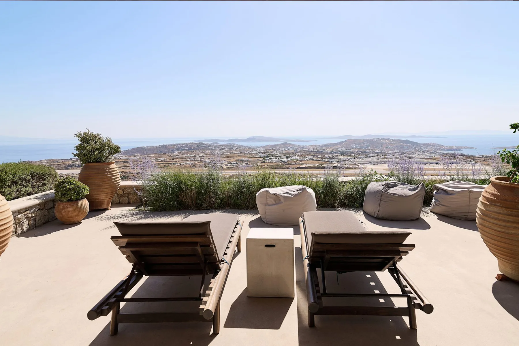 A sunny outdoor terrace overlooks a broad landscape, with loungers and planters.