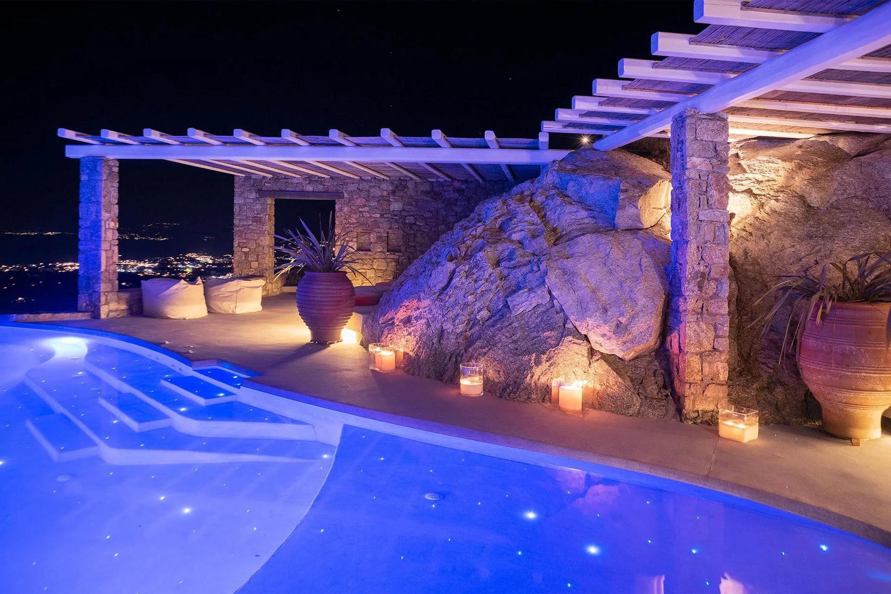 A brightly lit swimming pool beside a rocky outdoor patio at night.