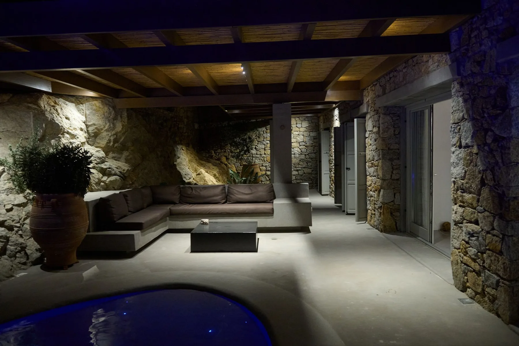 A covered stone patio with lounge seating and a small pool in the foreground.