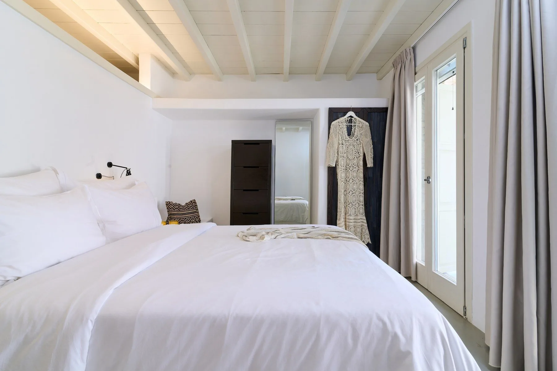 A bright bedroom with a neatly made bed and a tall window.