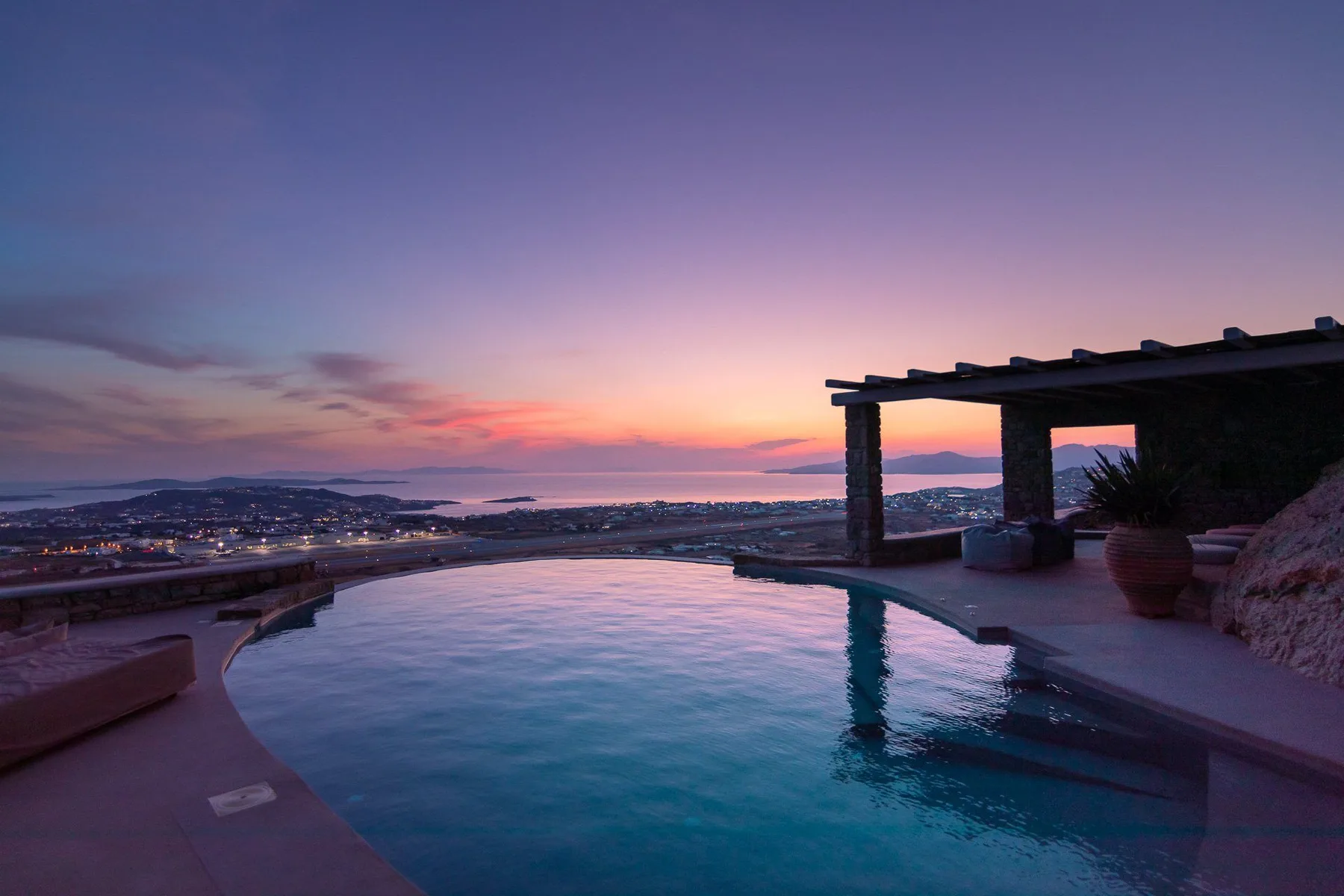 A swimming pool overlooks a coastal town at sunset.