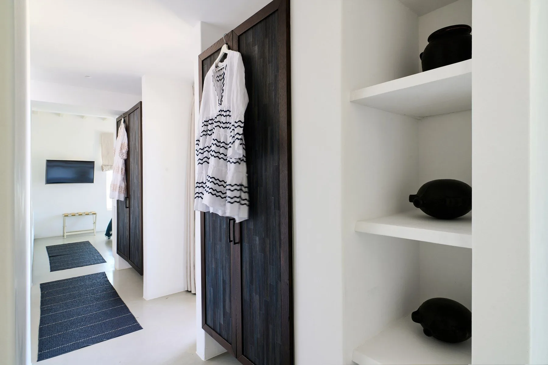 A bright hallway with dark doors and open wall shelves.