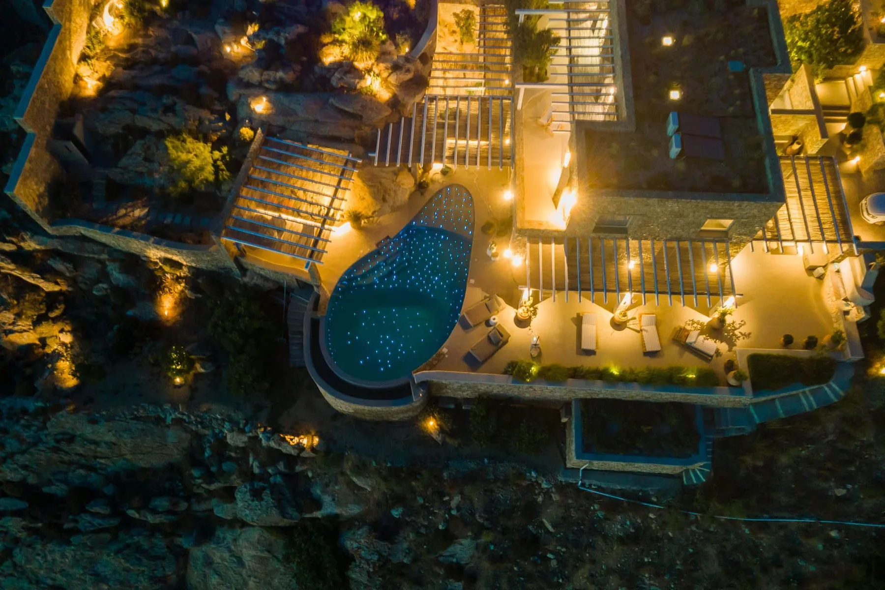 An illuminated outdoor pool and adjoining deck are shown at night.