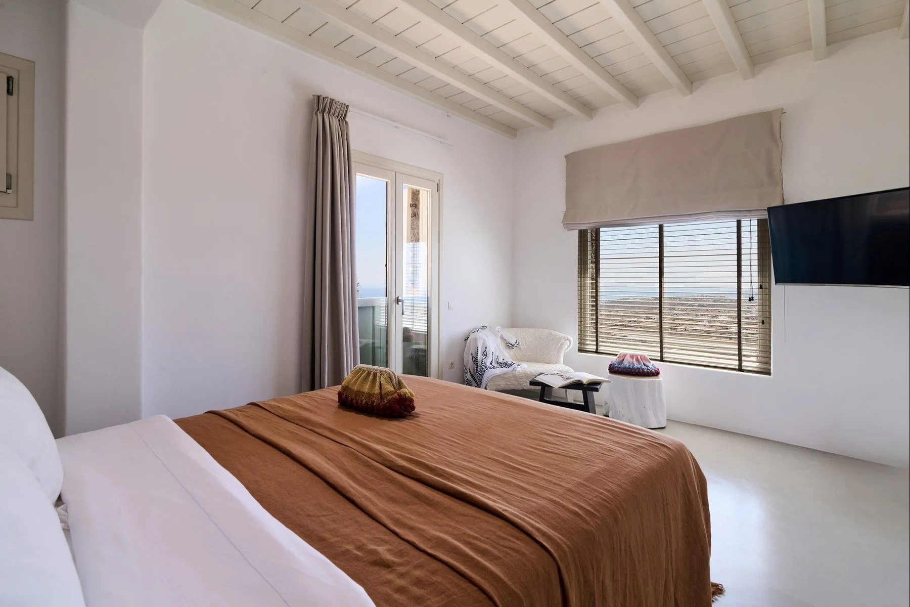 A bright bedroom with a bed, window, and television.