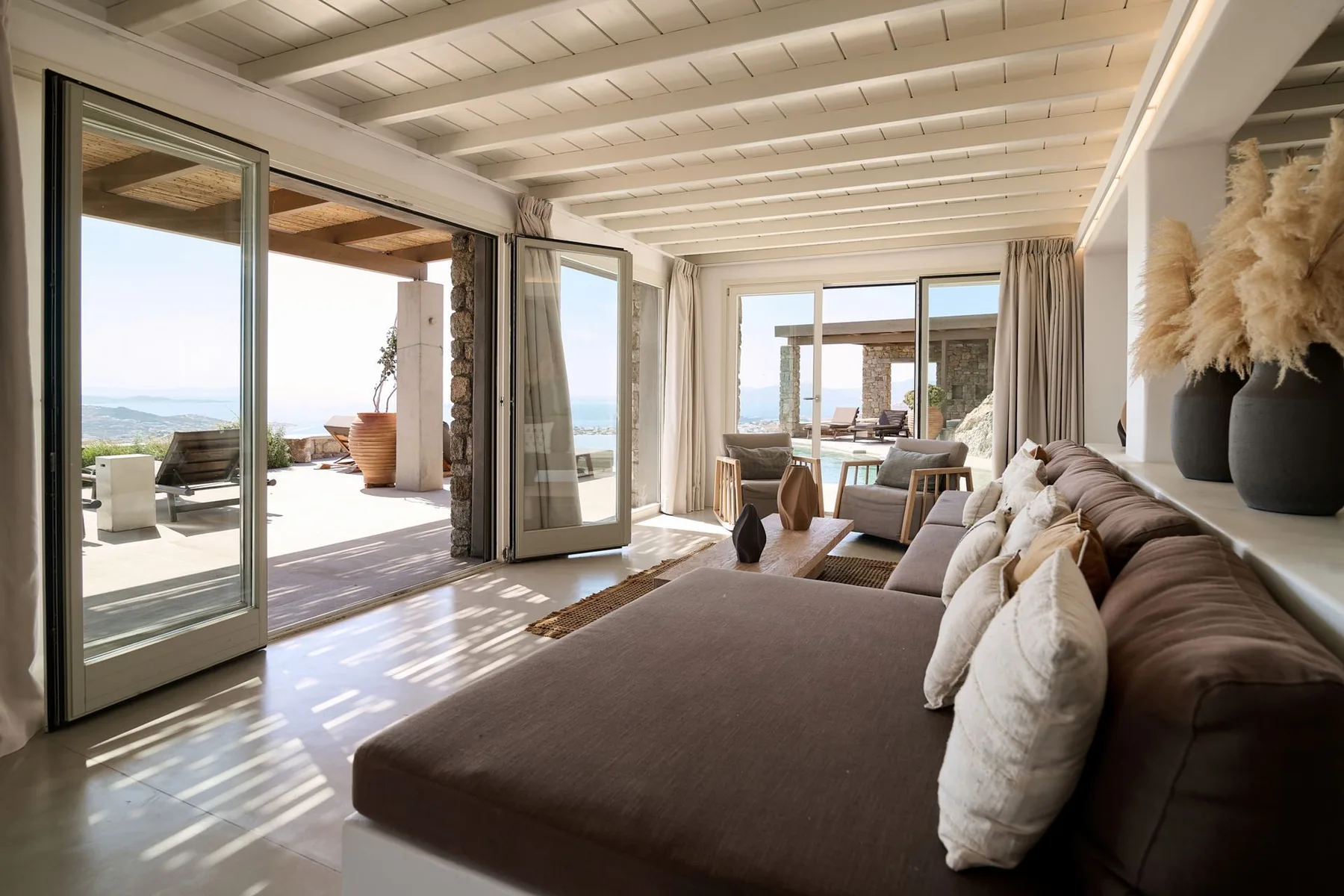 A bright living room opens onto a patio, with a large sofa facing the sea.