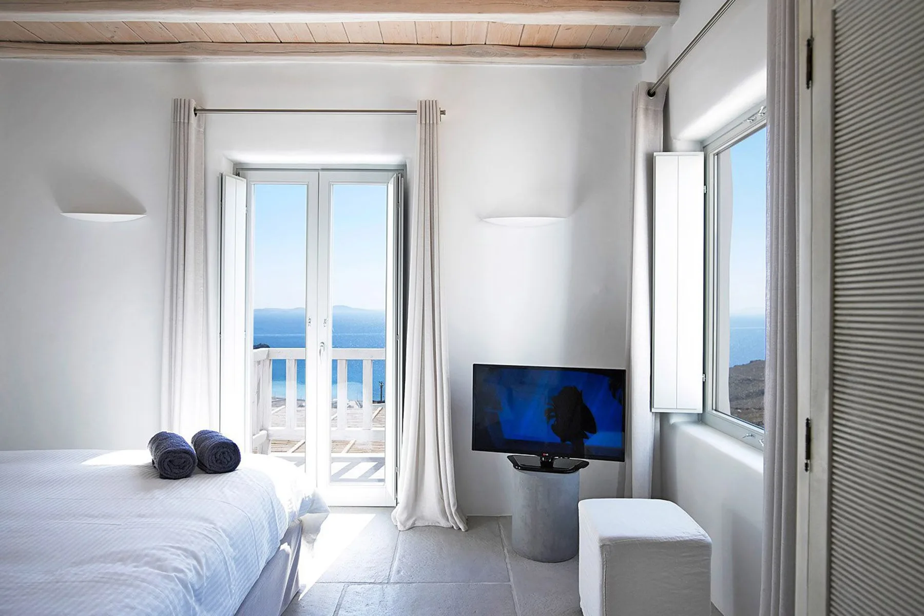 A bright bedroom opens onto a balcony, with a television beside the bed.
