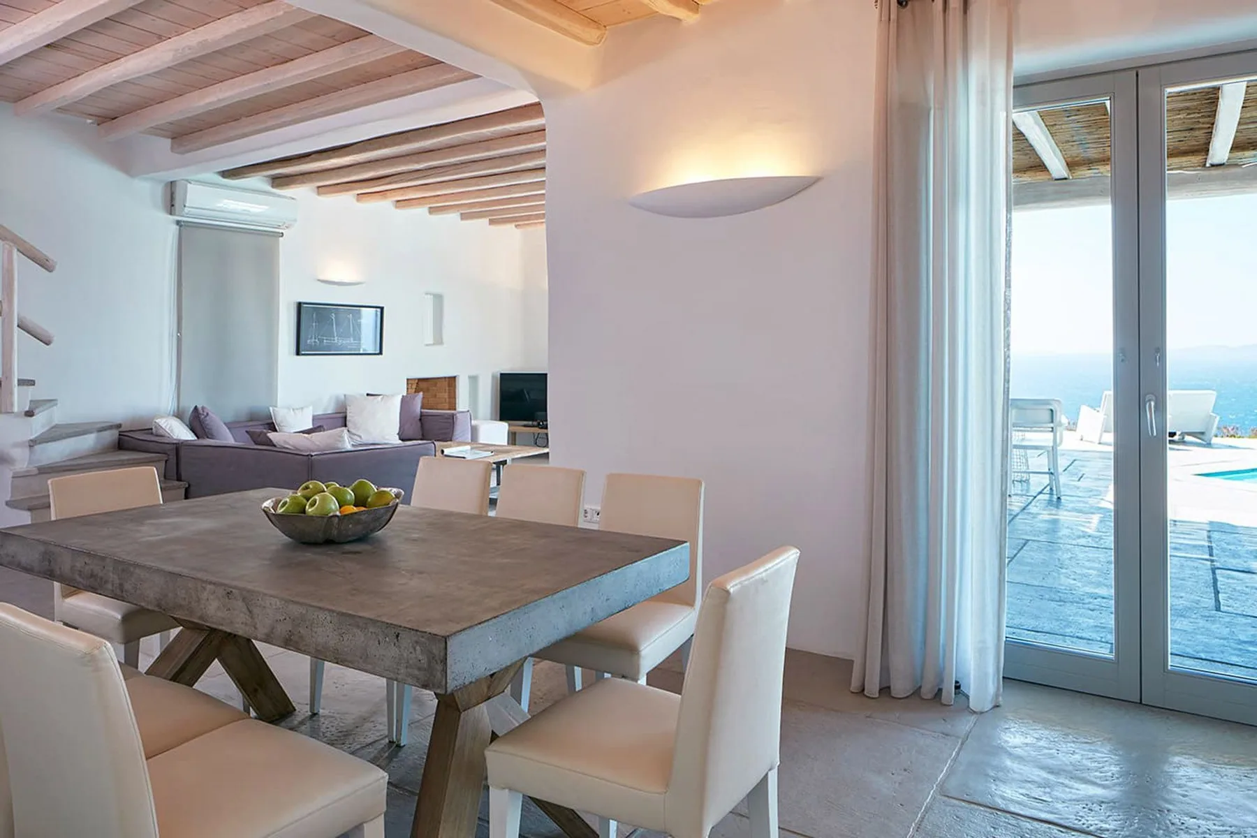 A dining area with a table and seating opens onto a bright living space.