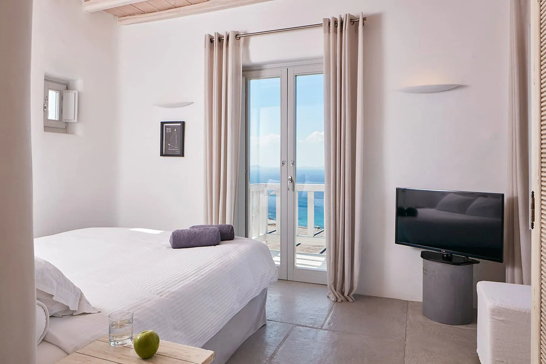 A bright bedroom with a bed and glass doors opening onto a sea view.
