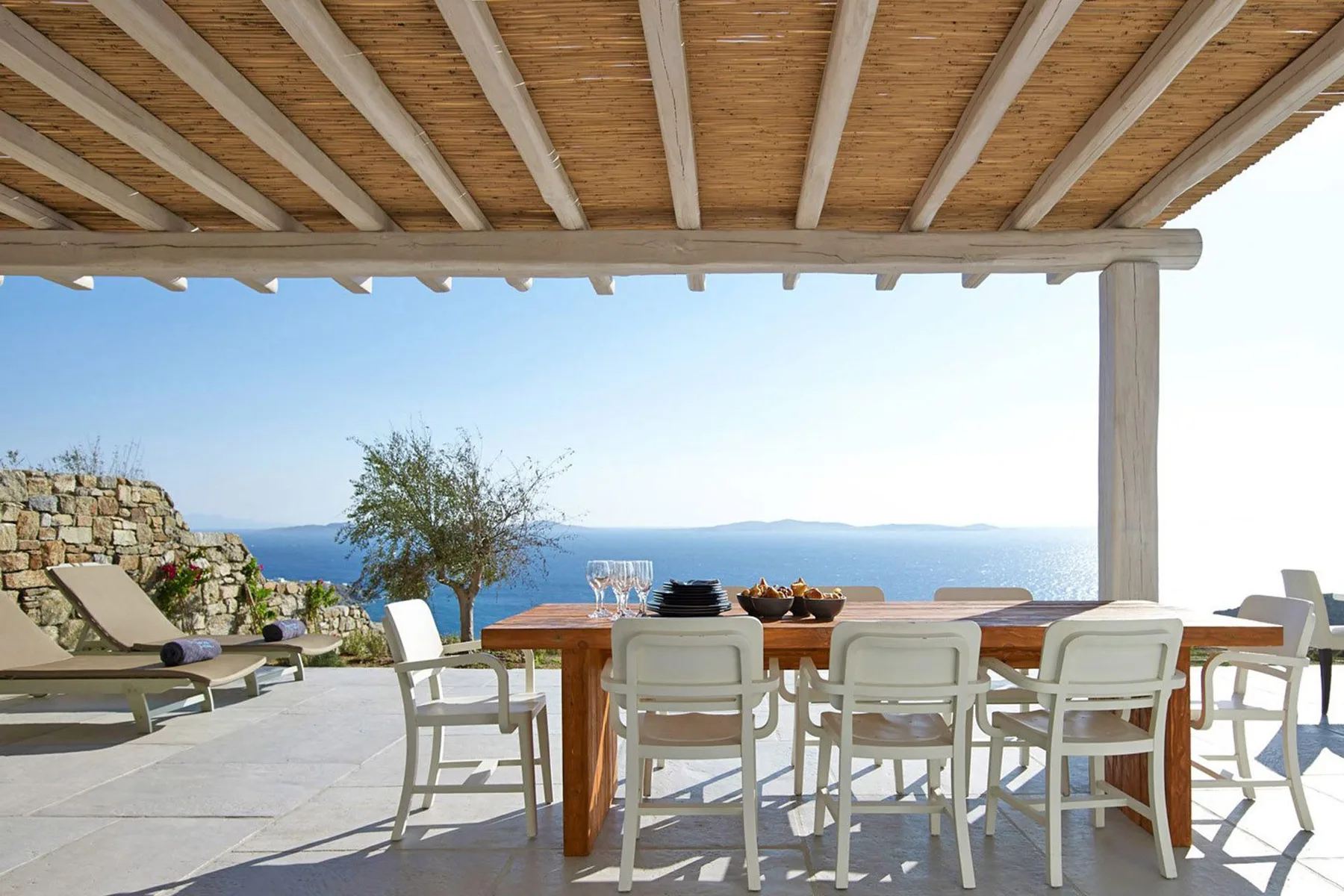 An outdoor dining area sits beneath a wooden pergola overlooking the sea.
