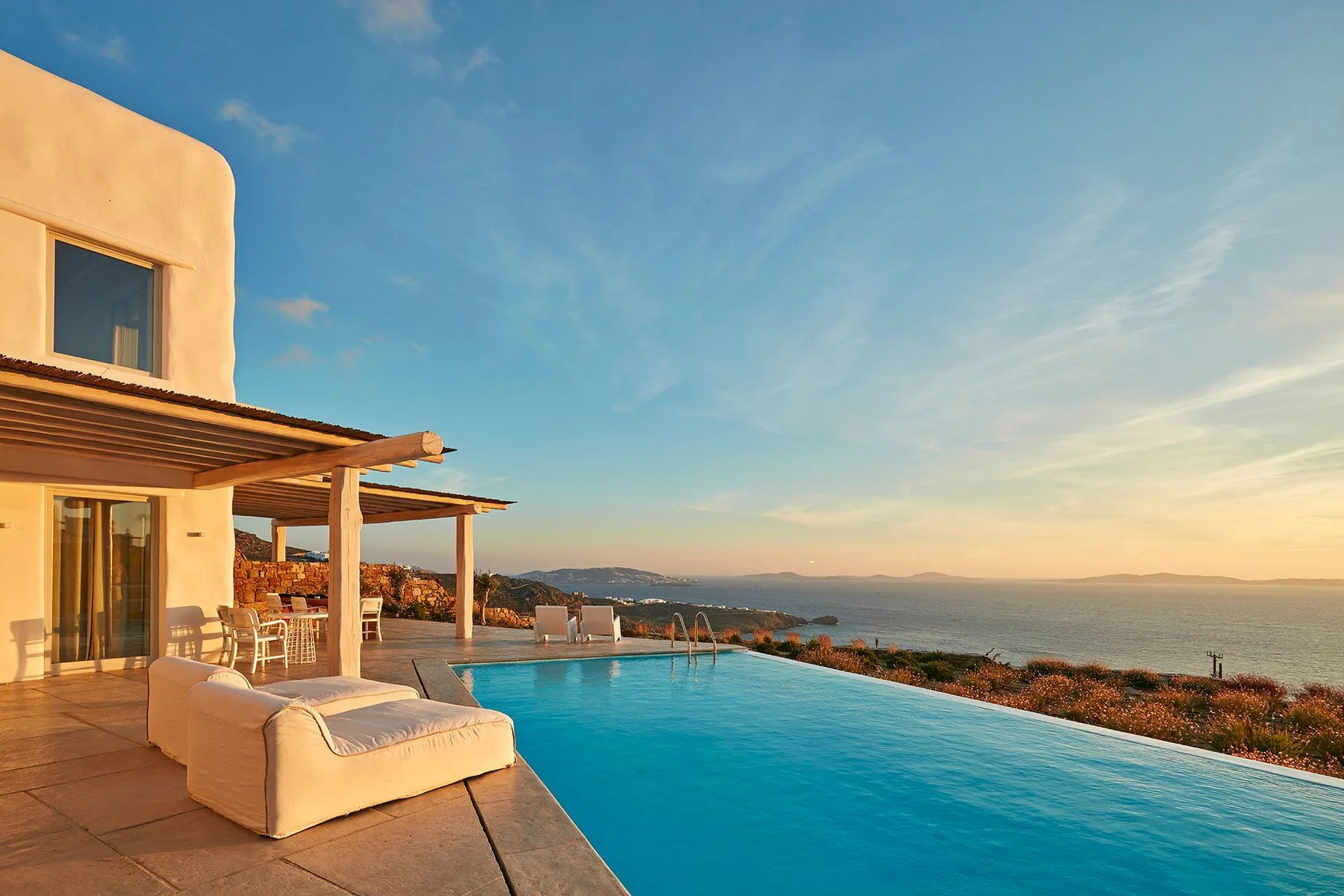 An outdoor pool beside a pale building overlooks the sea beneath a clear sky.