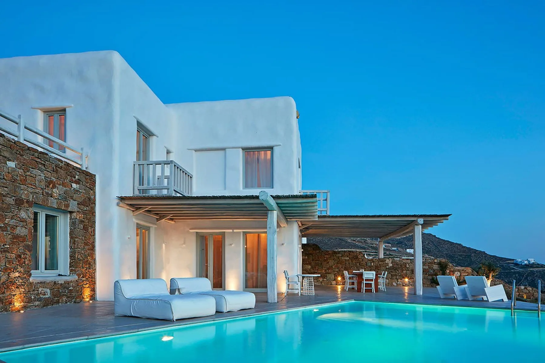 A modern white building opens onto a swimming pool and outdoor seating area.