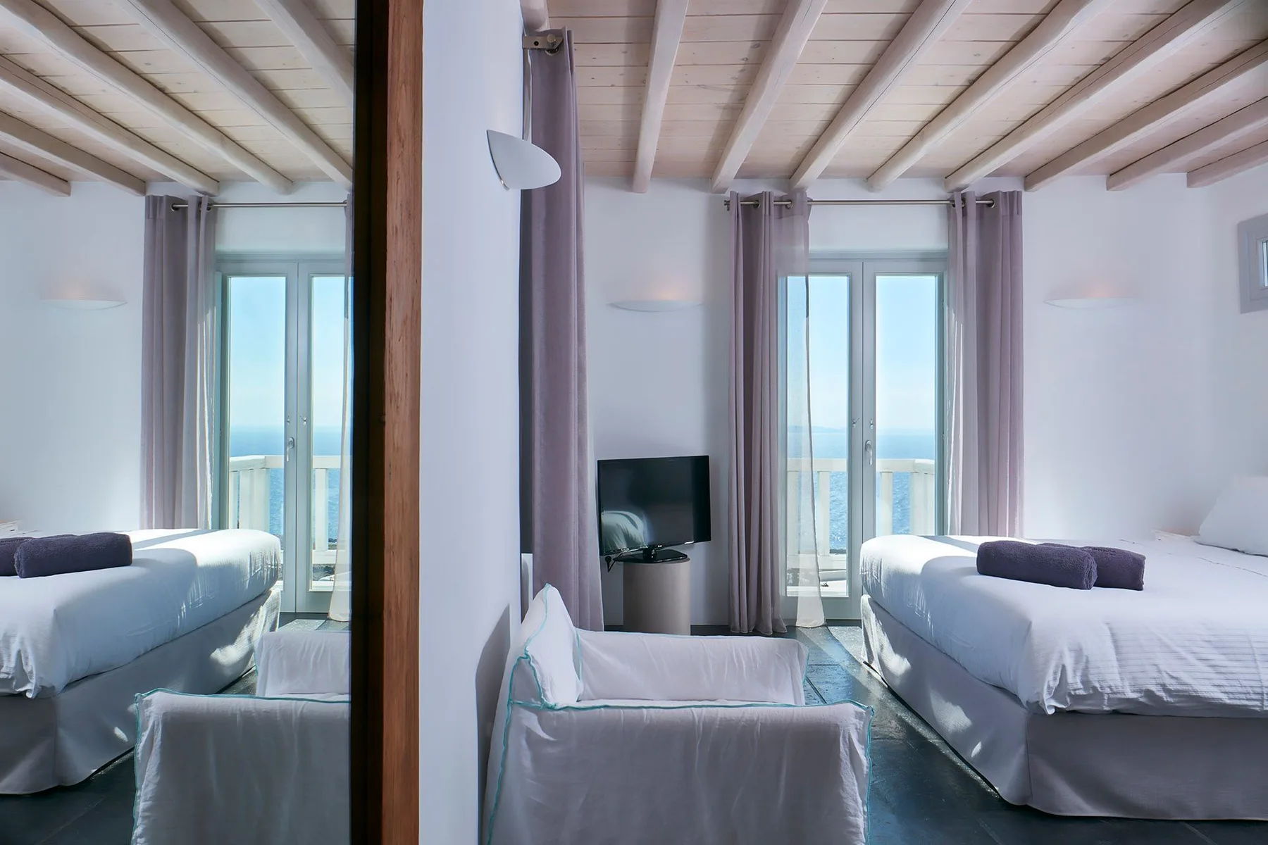 A bright bedroom with a bed, seating, and tall windows overlooking the water.