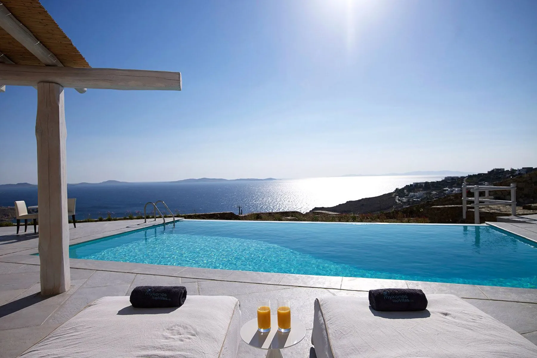 A swimming pool overlooks the sea, with sun loungers in the foreground.