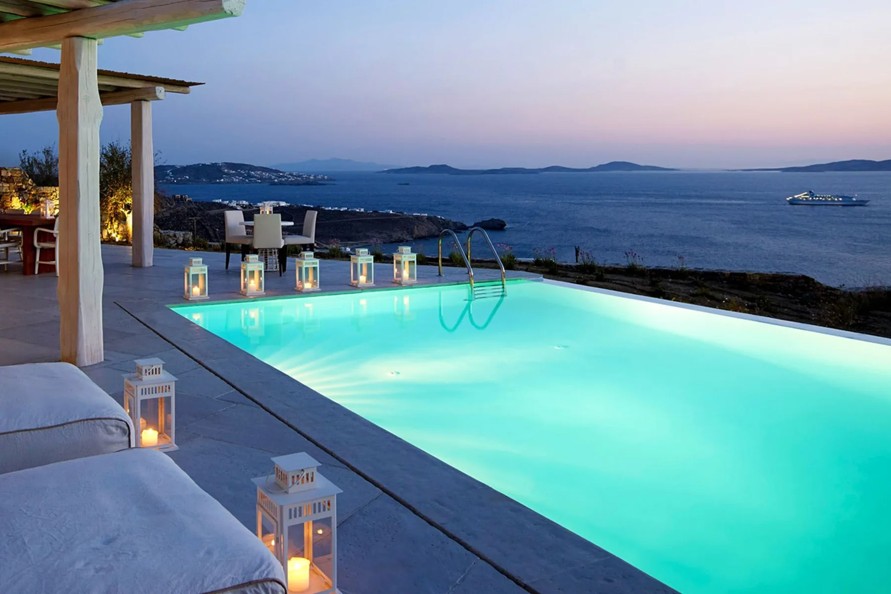 An illuminated swimming pool overlooks the sea at dusk.