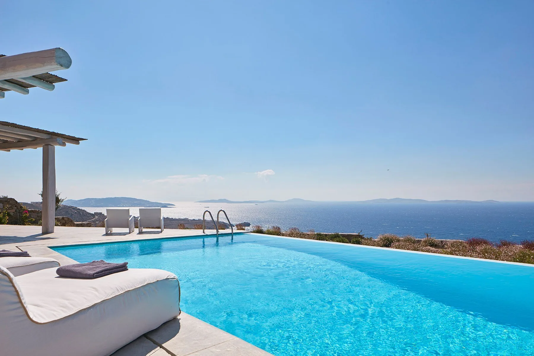 An outdoor swimming pool overlooks the sea, with cushioned seating beside it.