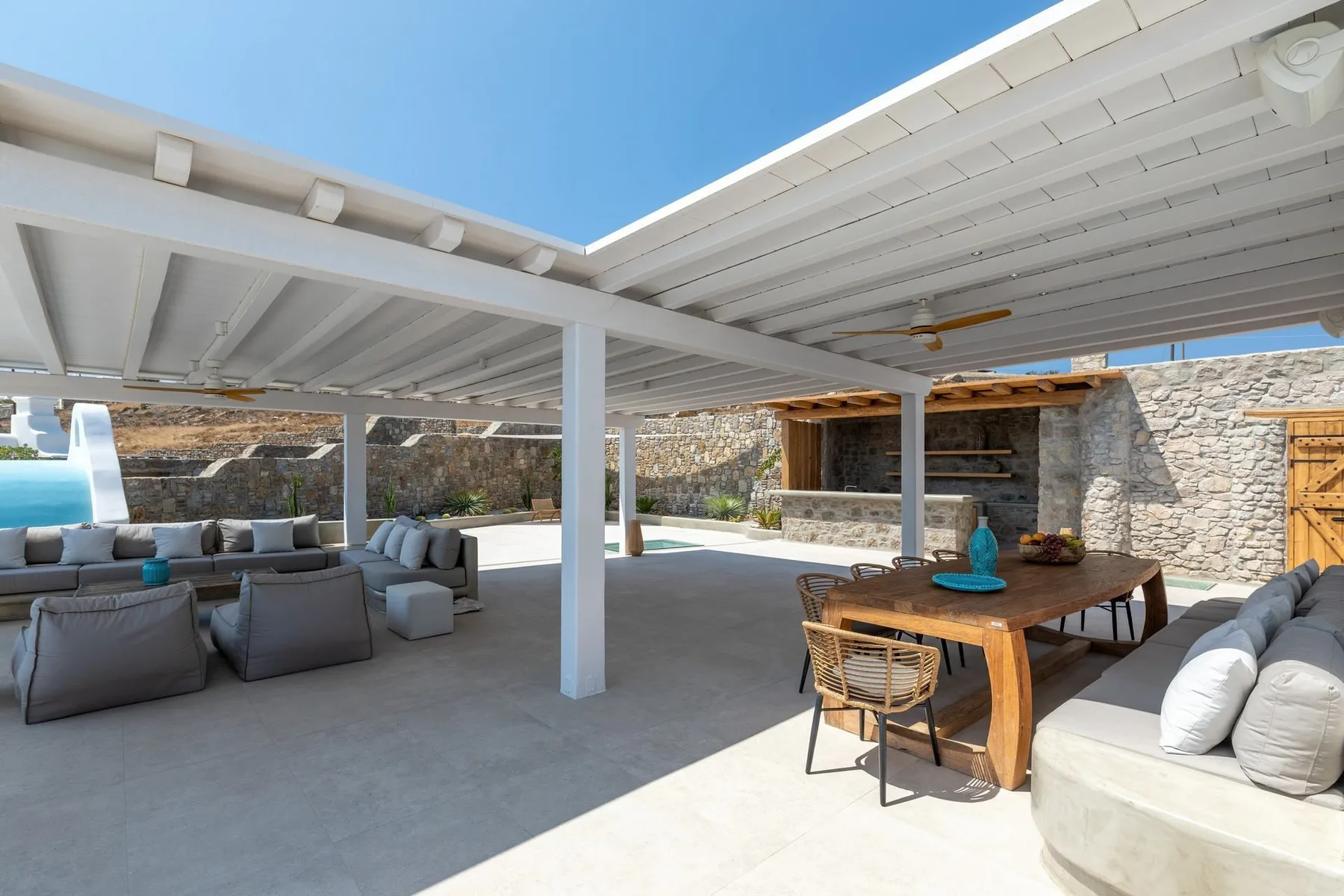 A covered outdoor patio with lounge seating and a wooden dining table.