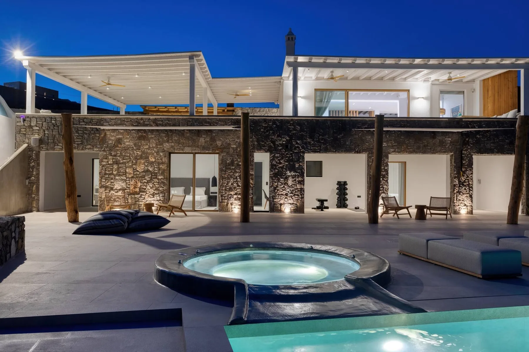 A modern outdoor pool courtyard is lit at dusk, with a circular spa and lounge seating.