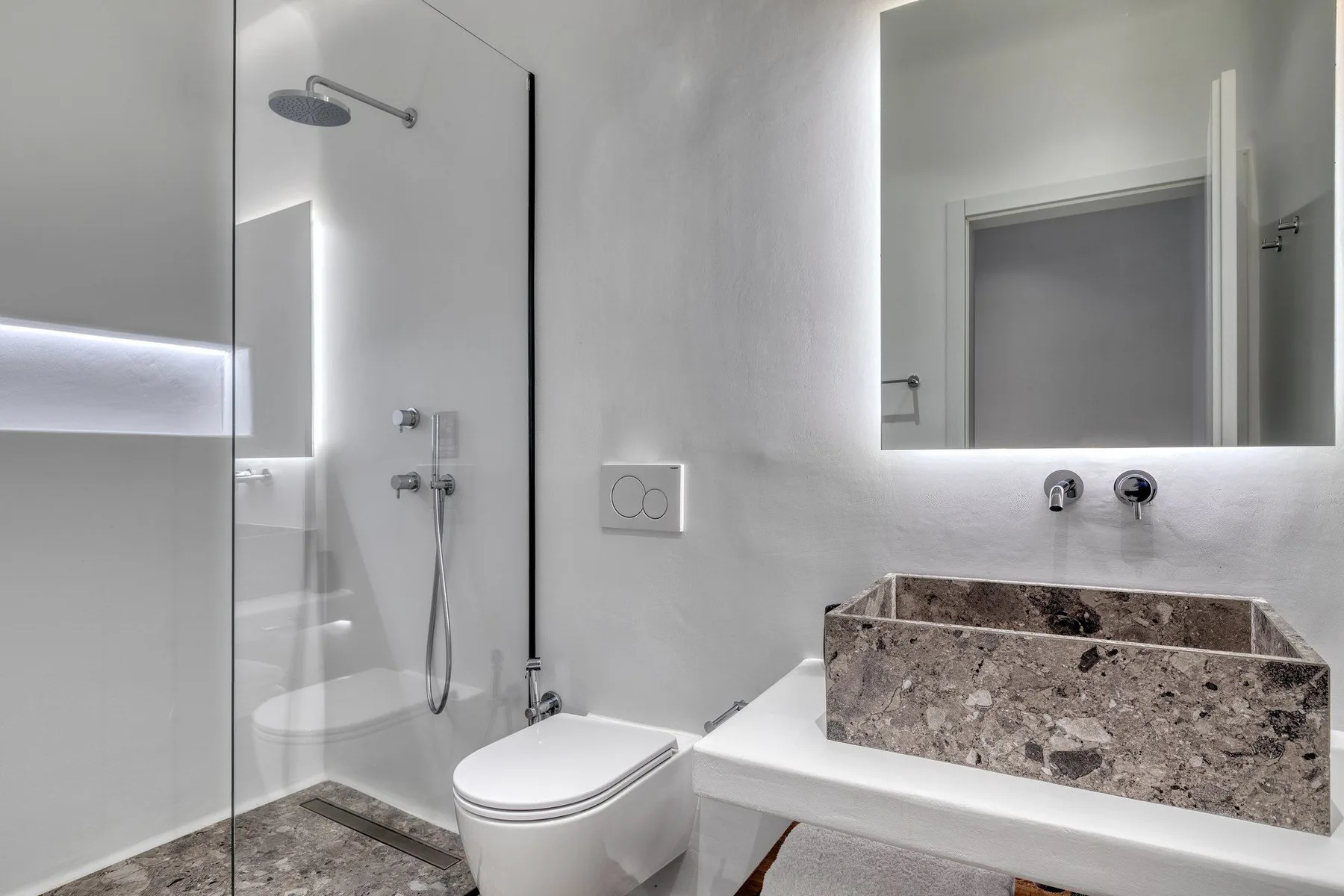 A modern bathroom with a glass shower, toilet, and stone basin beneath a large mirror.