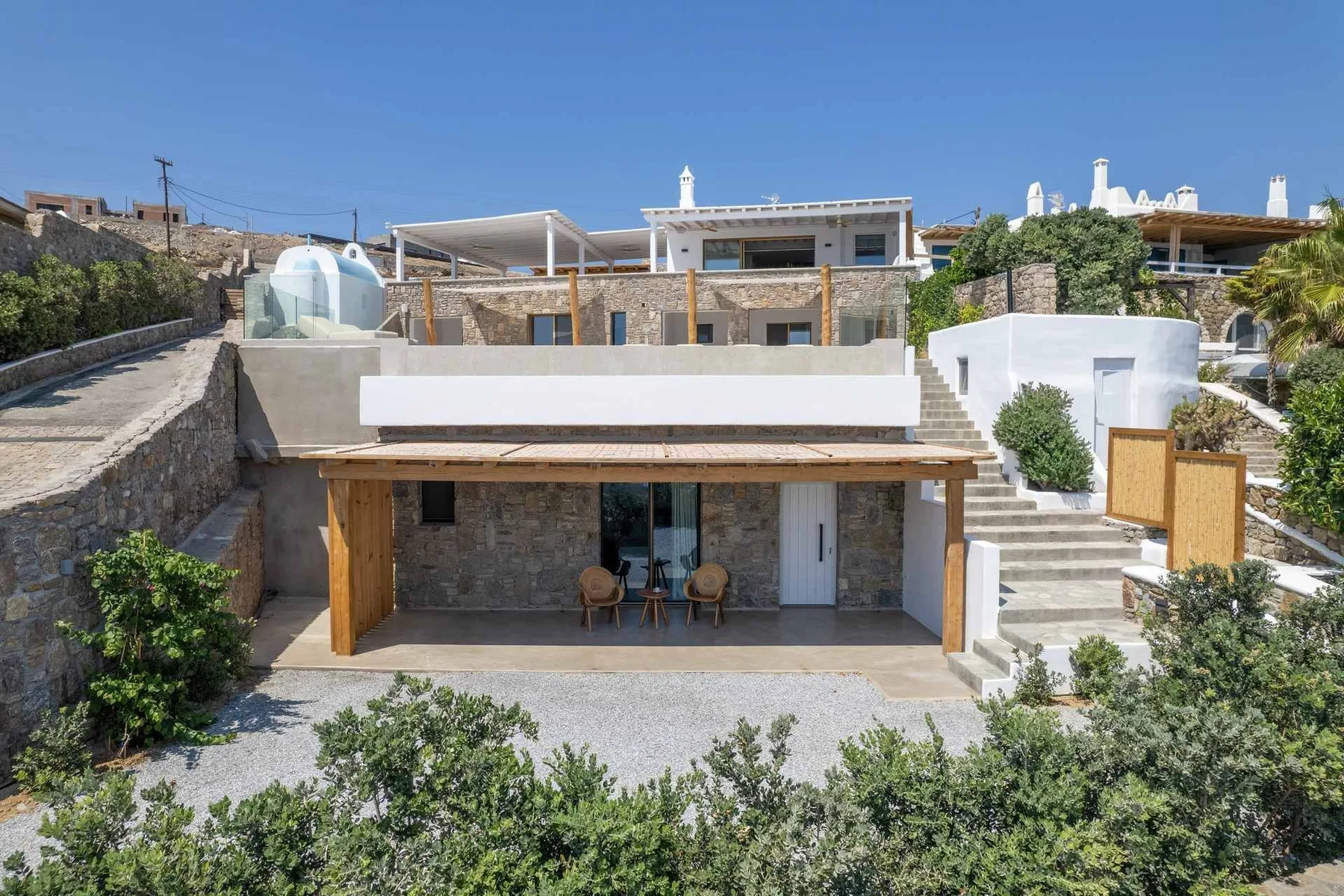 A modern stone house with a shaded patio and outdoor seating.