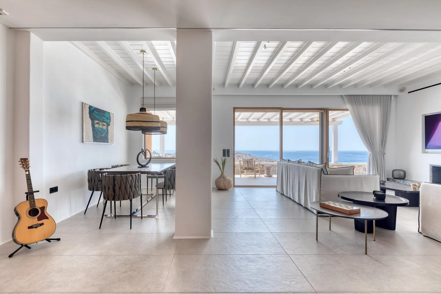 An open-plan living and dining area looks out through glass doors toward the sea.