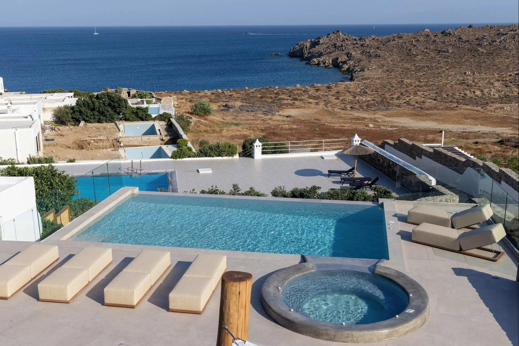 A coastal pool terrace overlooks the sea, with a round spa beside the pool.