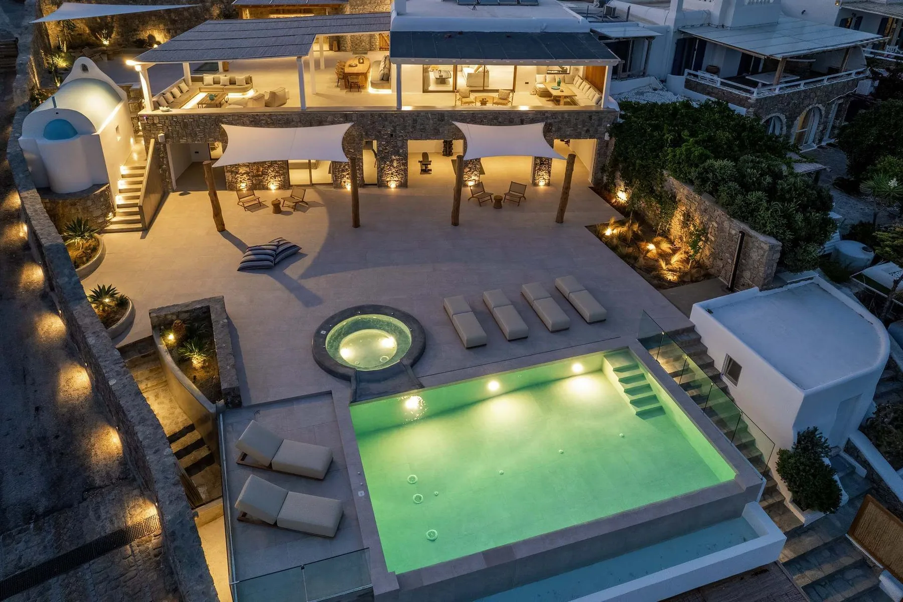 An illuminated outdoor pool and patio sit below a covered seating area.