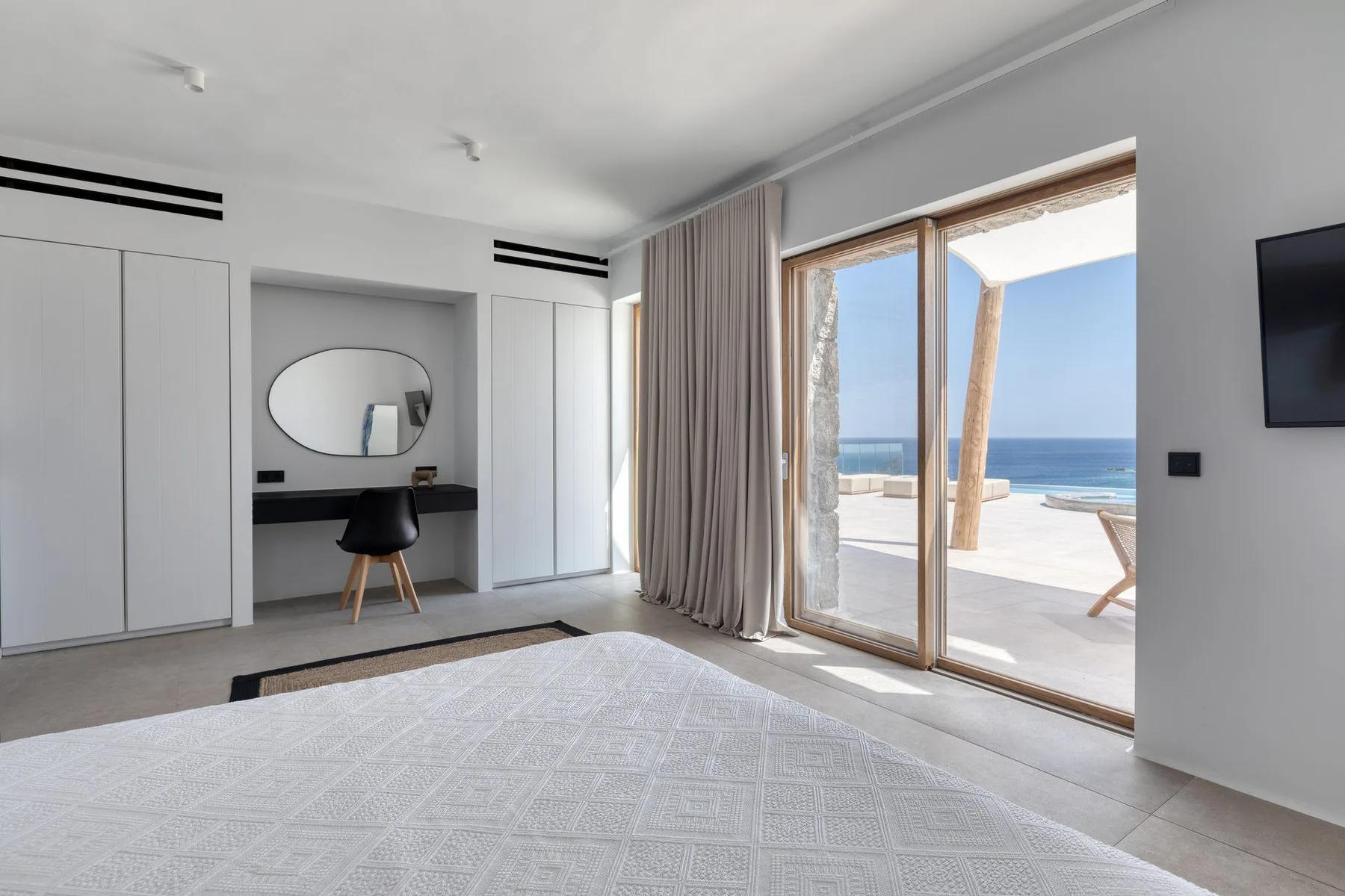 A bright bedroom with a desk and sliding glass doors opening onto an ocean view.