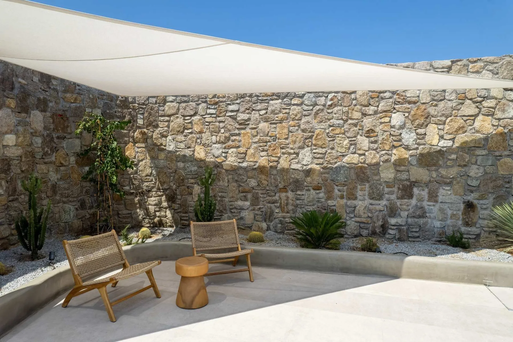 A stone-walled outdoor patio with seating beneath a shade canopy.
