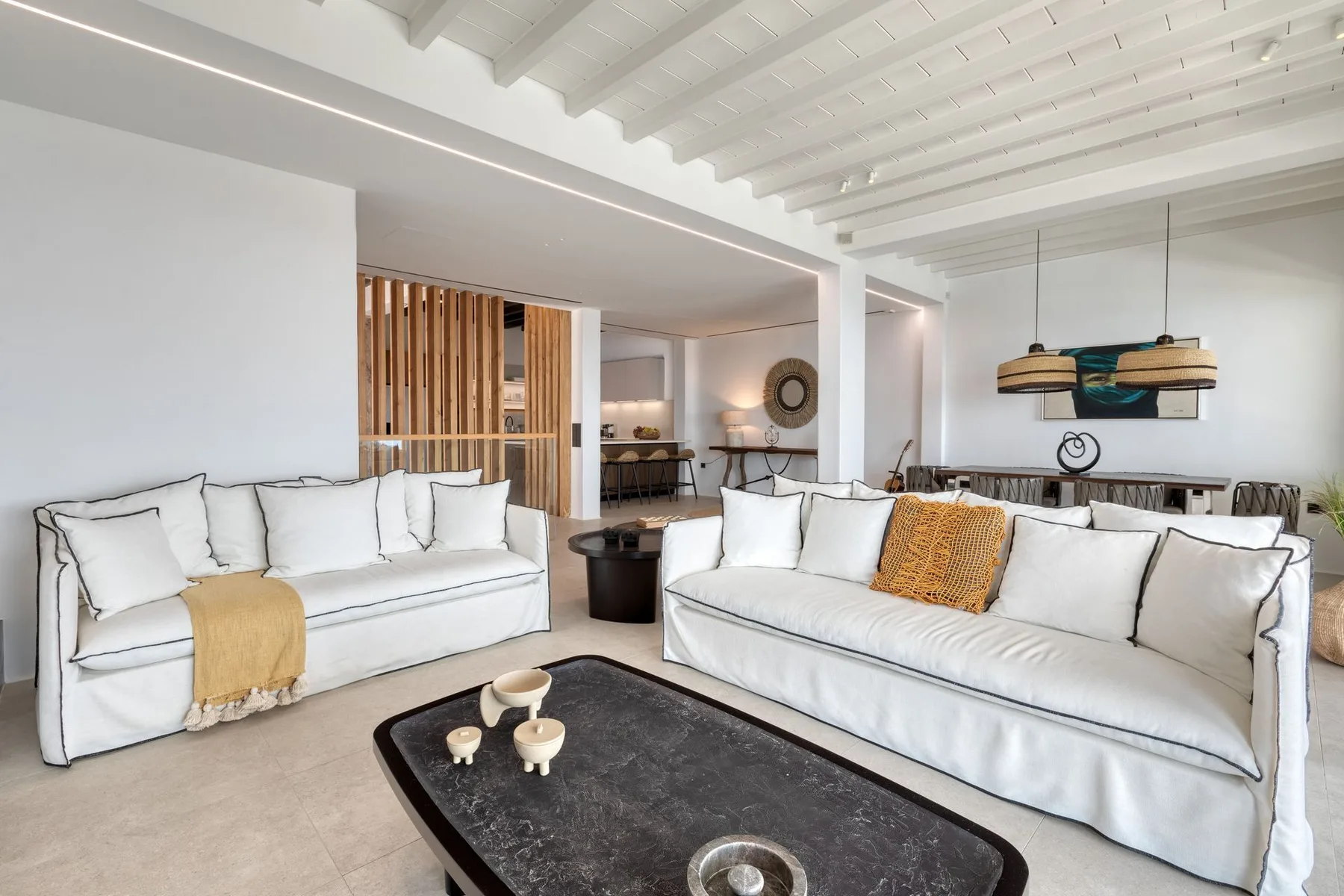 A bright living room with white seating, a dark coffee table, and exposed ceiling beams.