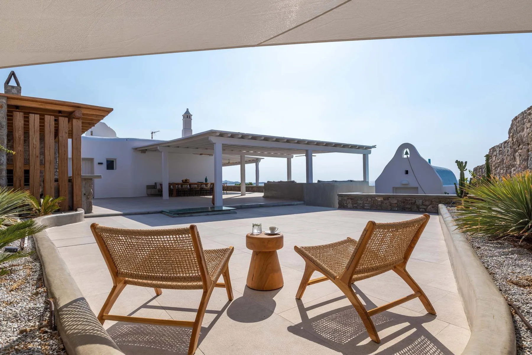 A sunlit outdoor terrace has woven seating and a table beneath a pergola.
