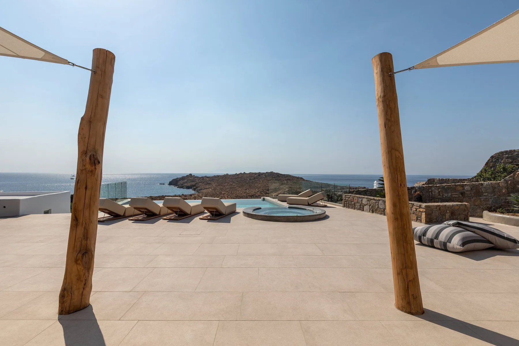 A sunlit terrace overlooks the sea, with loungers and a small round pool.