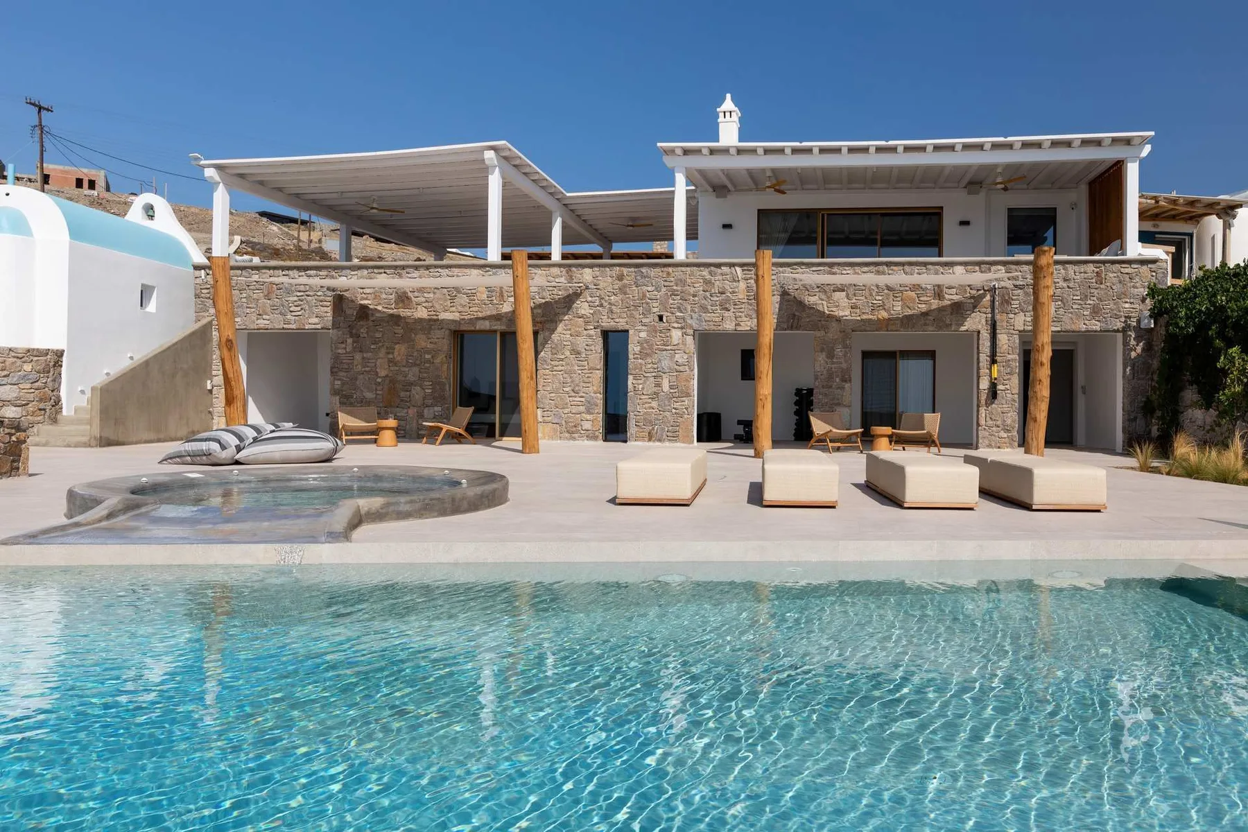 A modern stone house overlooks a swimming pool and sun loungers.