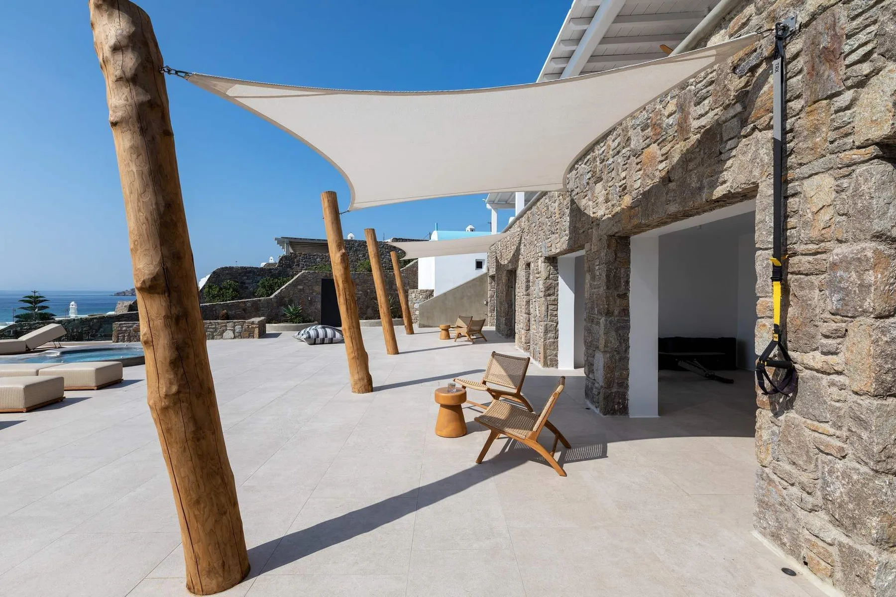 A sunlit stone terrace with shaded seating and a view of the sea.