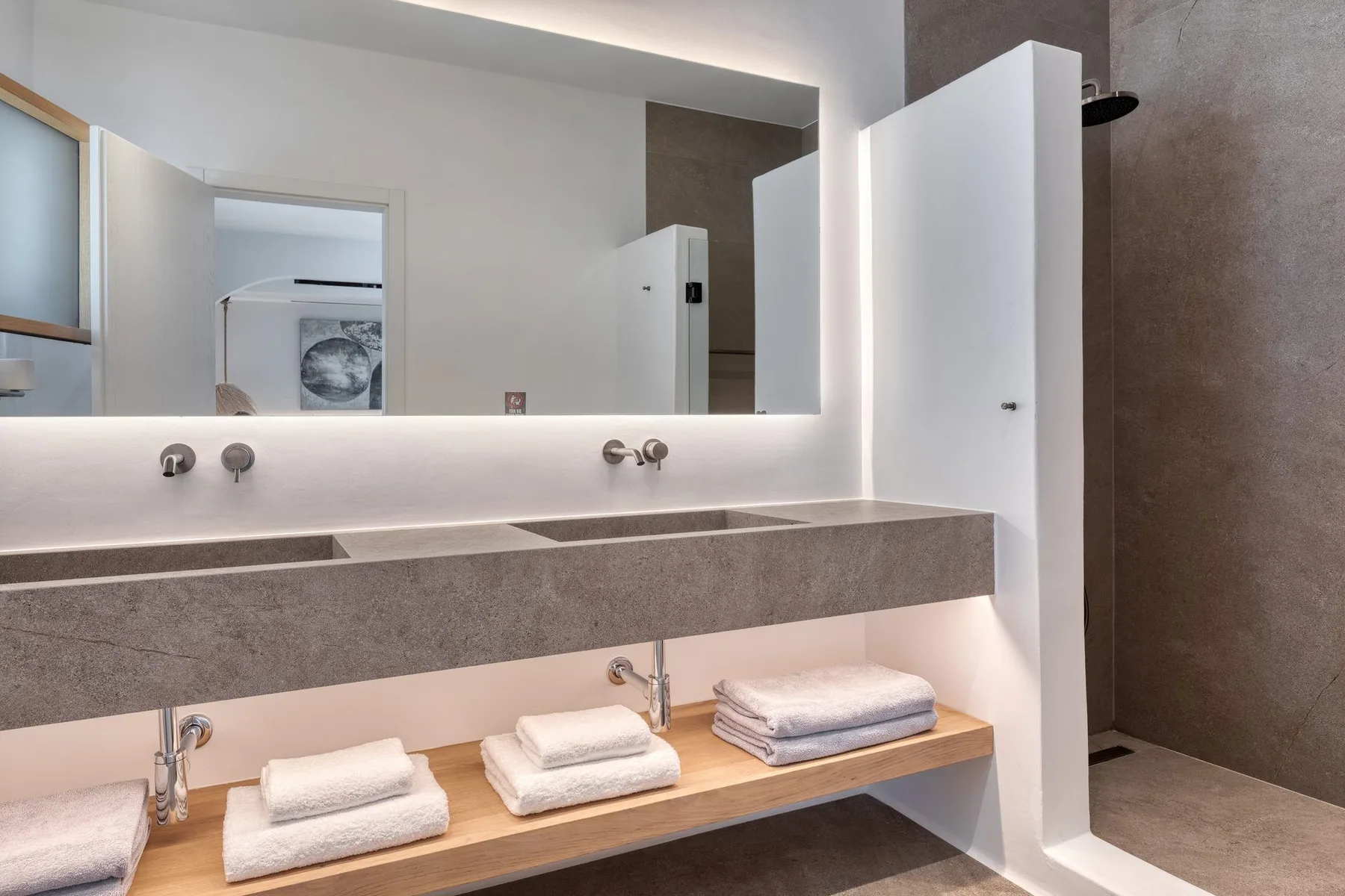 A modern bathroom vanity with a long counter, wall-mounted faucets, and folded towels.