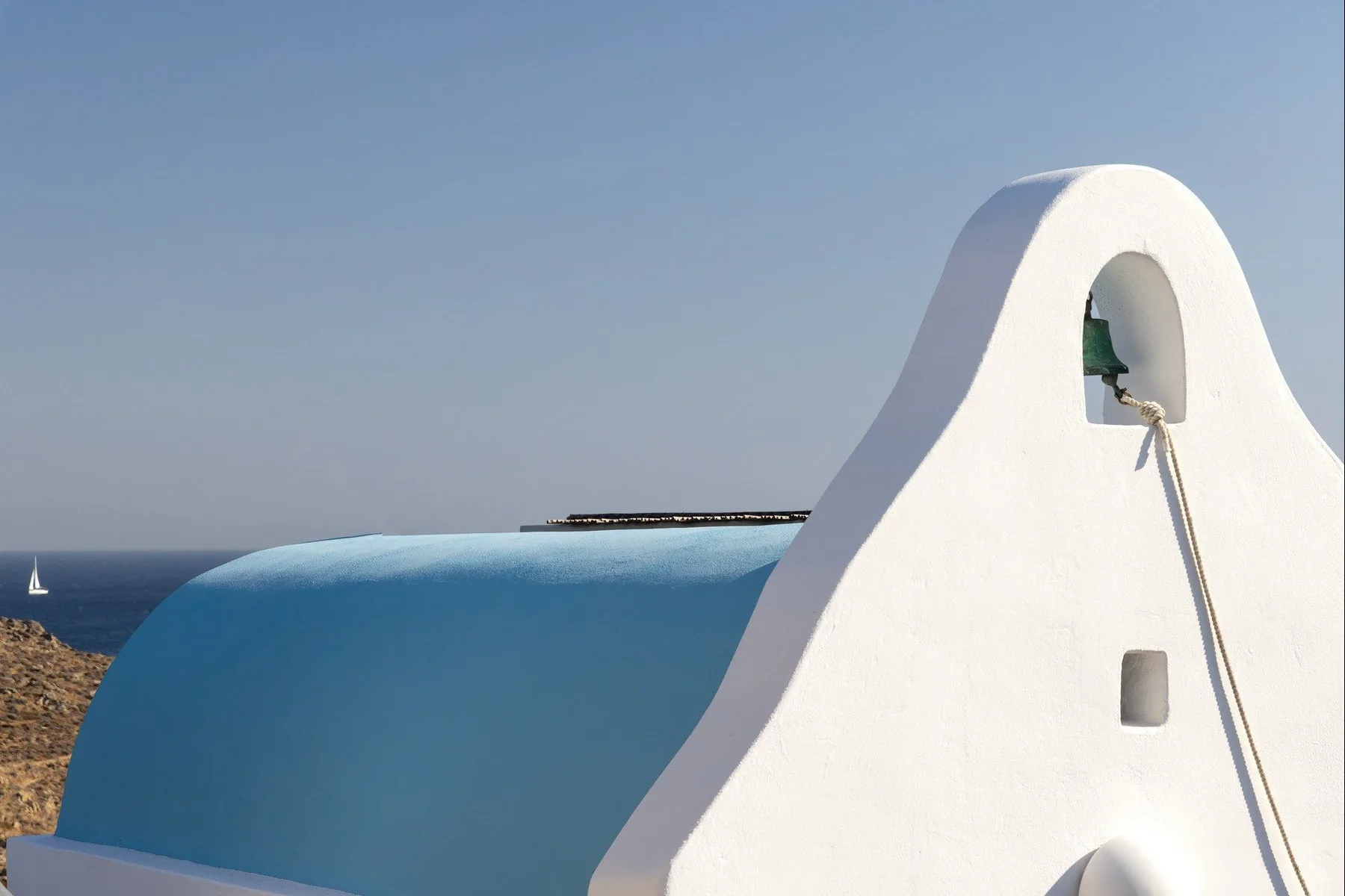 A white sculptural exterior wall overlooks the sea beneath a clear sky.