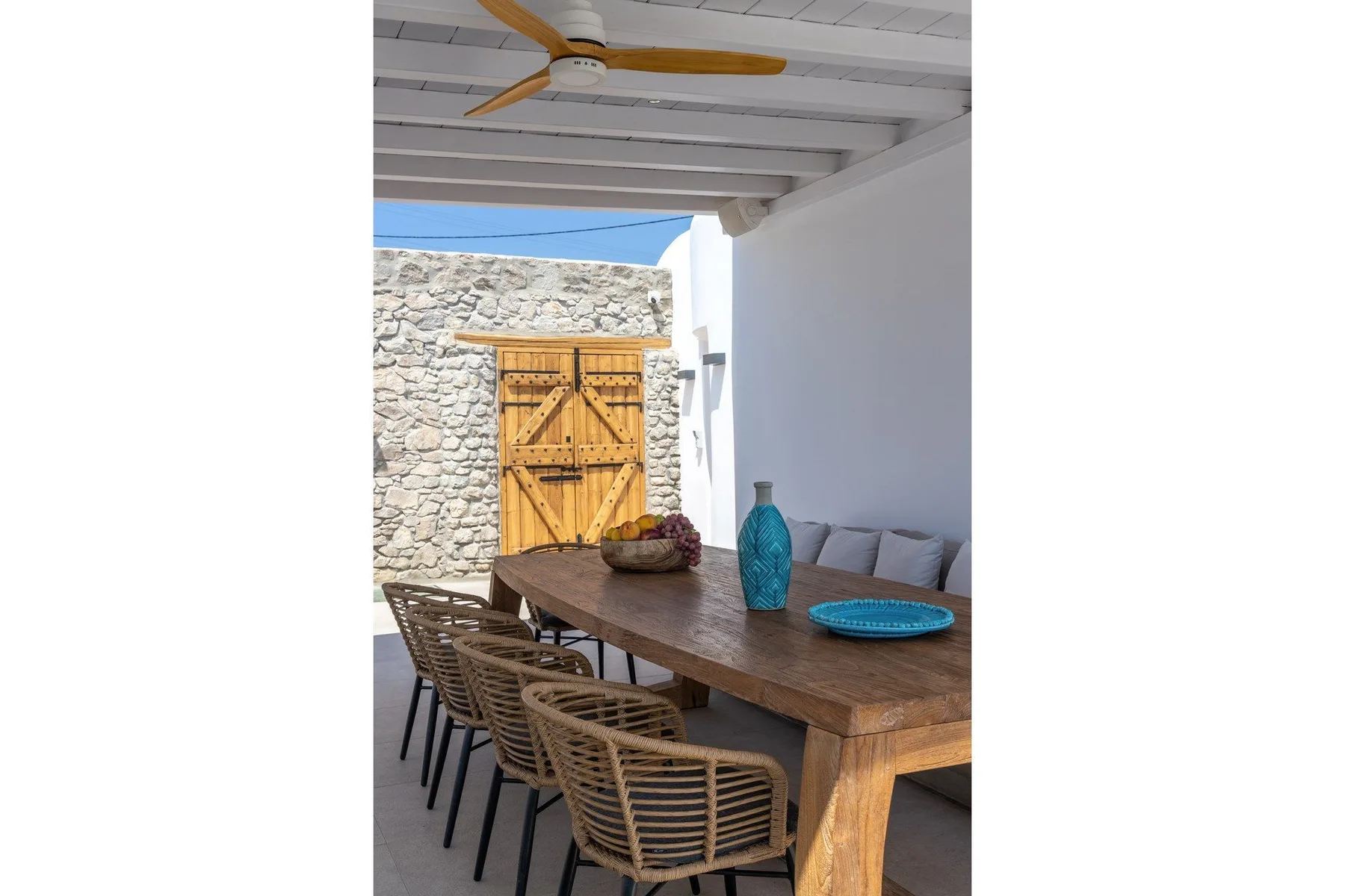 A covered outdoor dining area with a wooden table and woven seating.