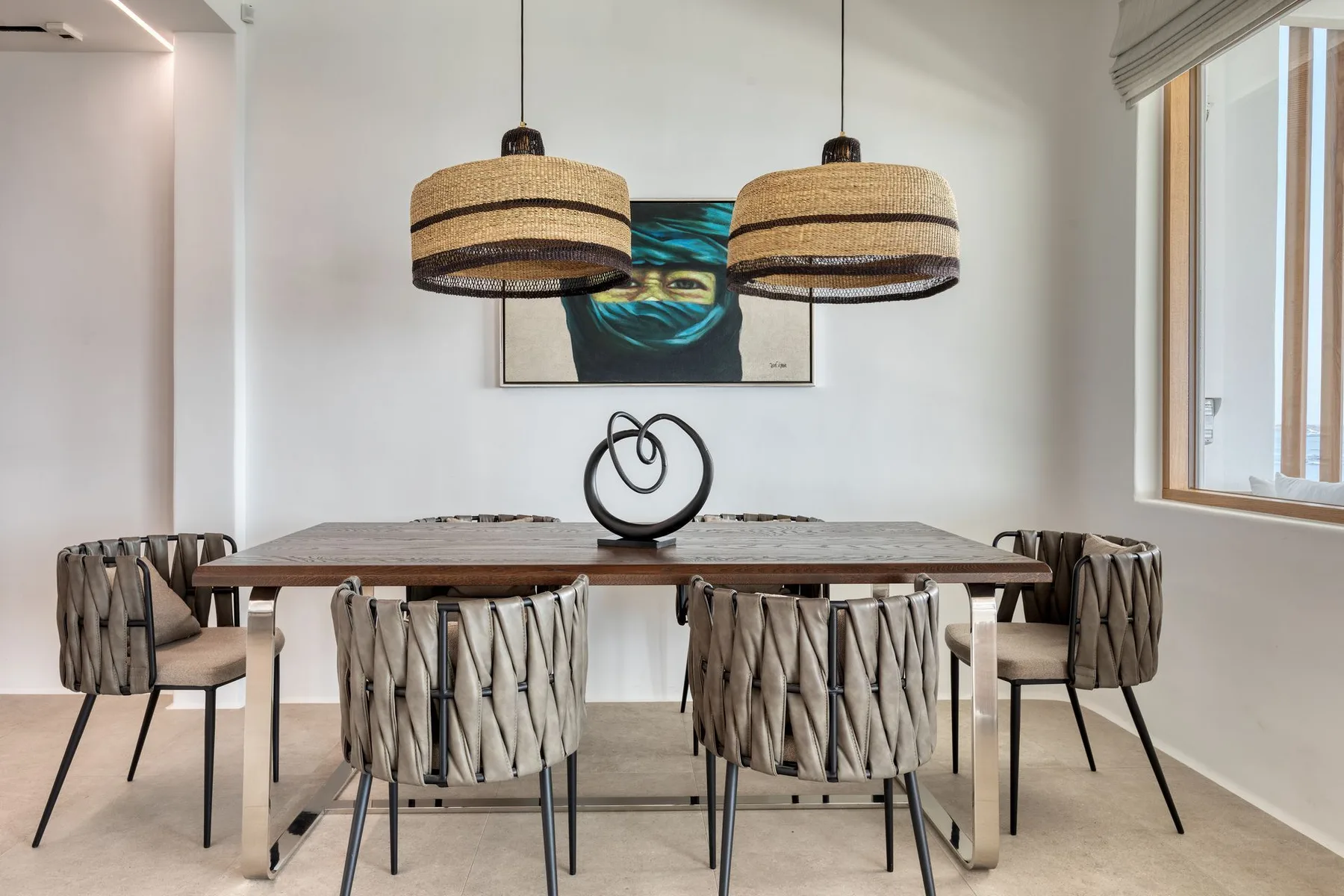 A dining area features a long table, surrounding chairs, and two woven pendant lights.