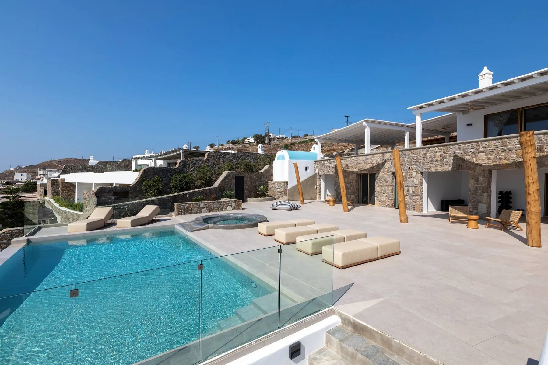 An outdoor pool sits beside a spacious paved terrace and modern buildings.