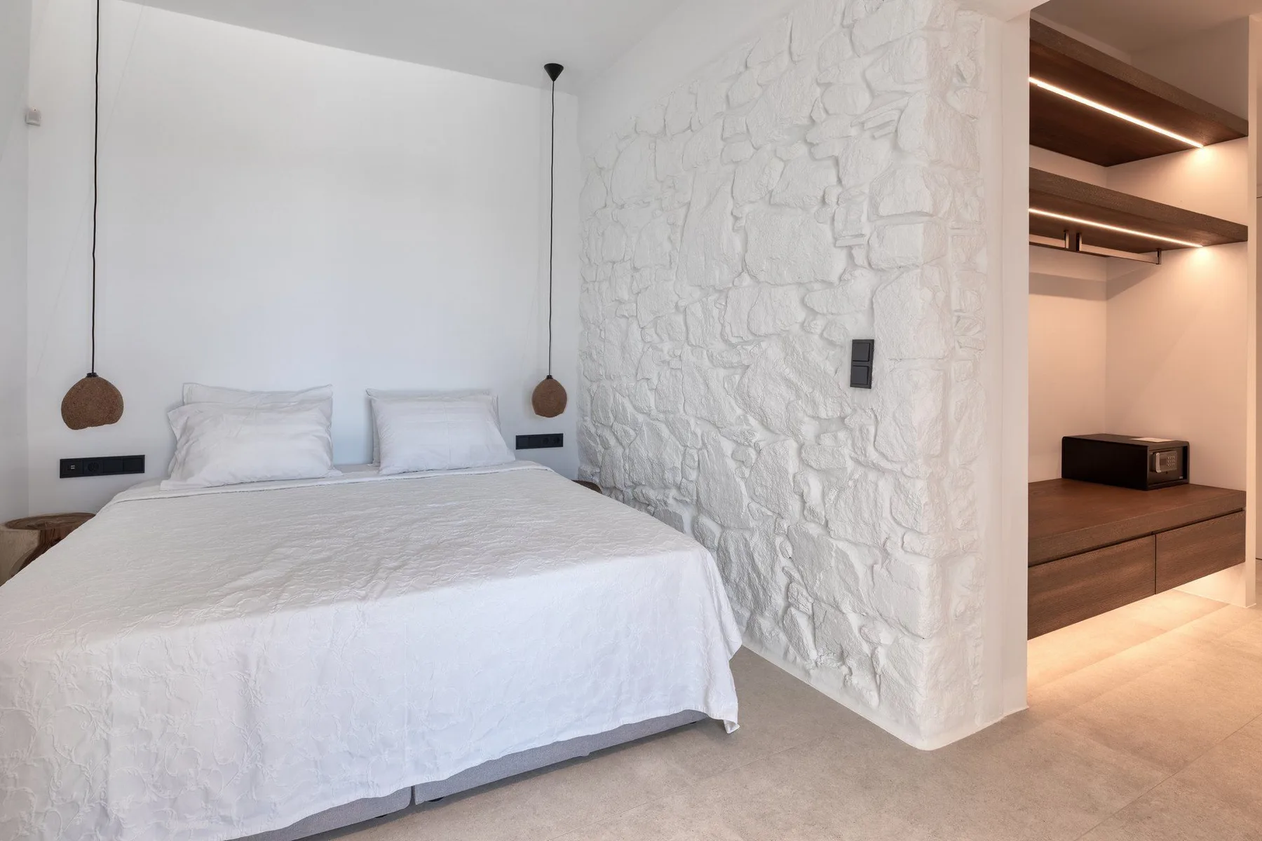 A bedroom with a white bed beside a white stone-textured wall.
