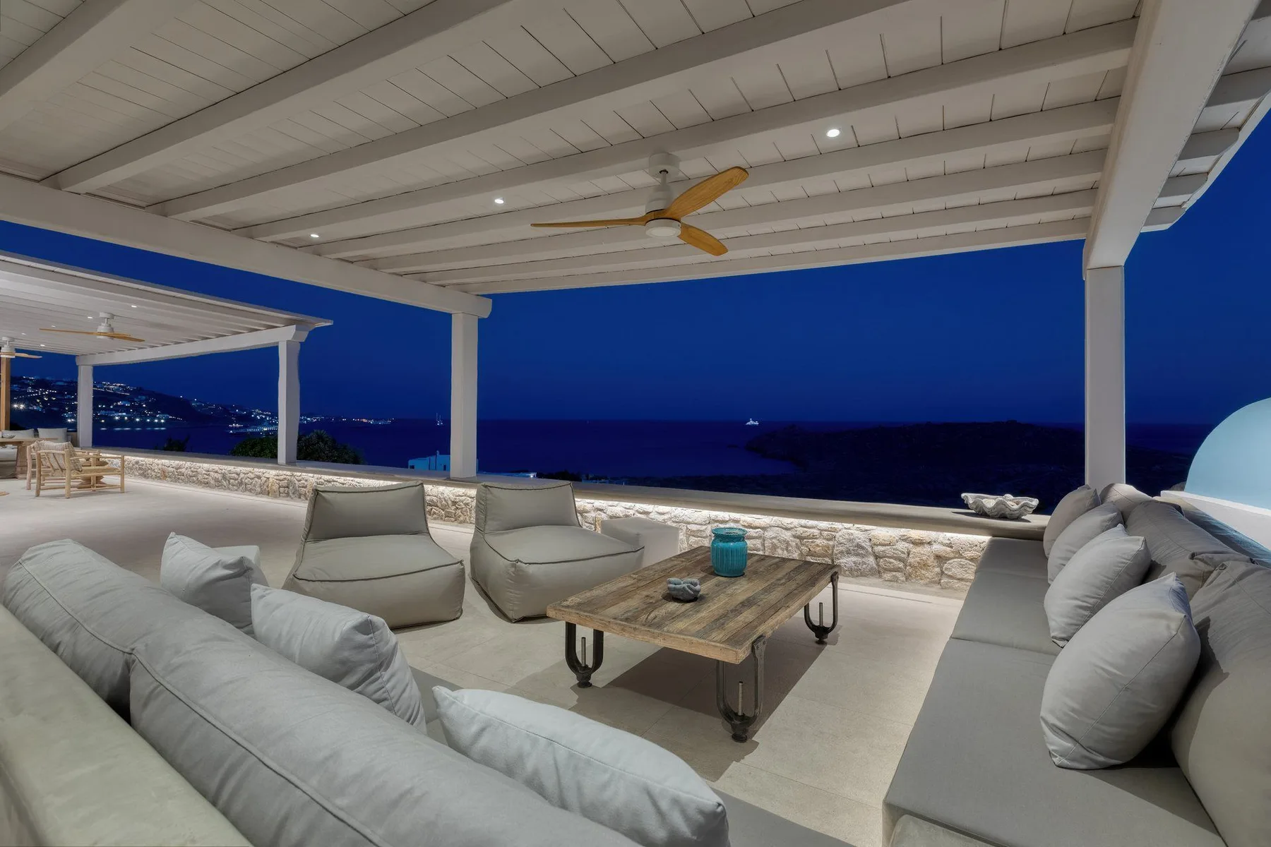 A covered outdoor lounge faces the sea, with cushioned seating and a low table.