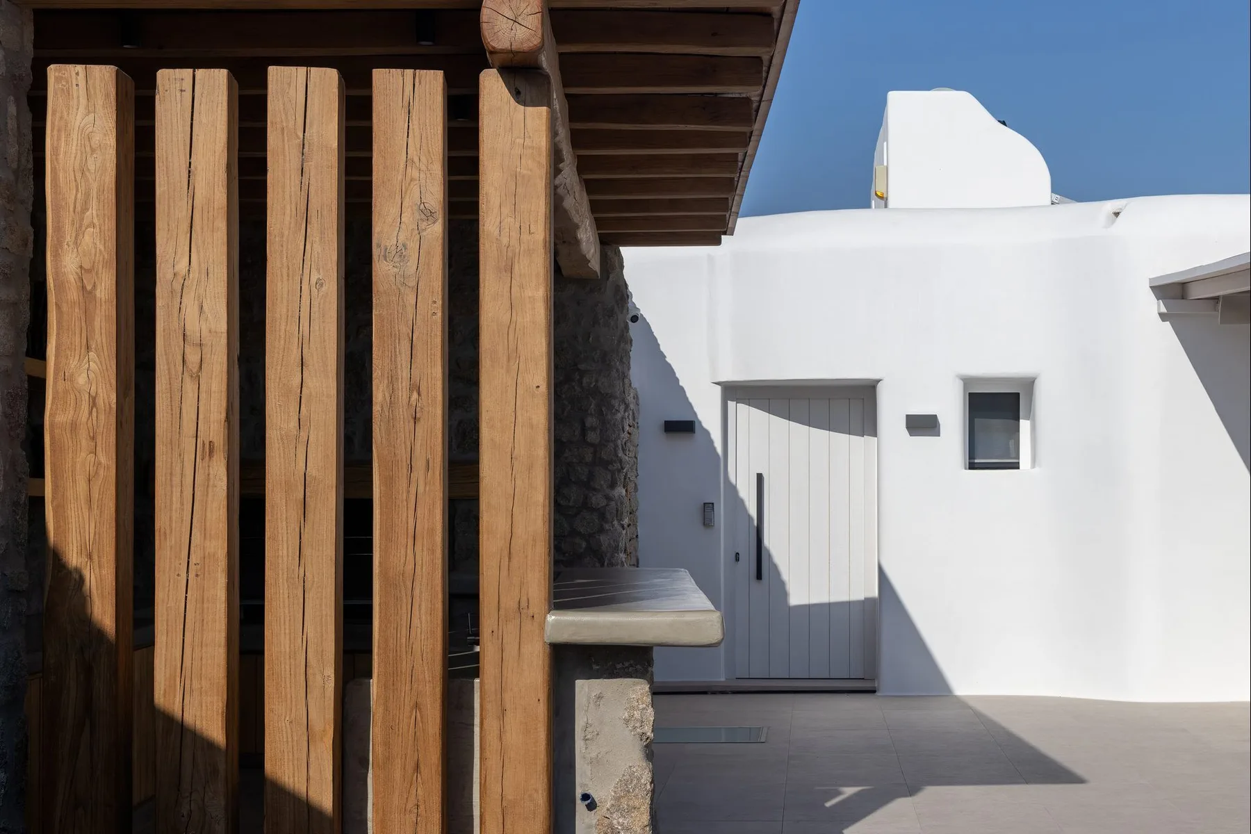 A white exterior entrance stands beside a shaded wooden slatted screen.
