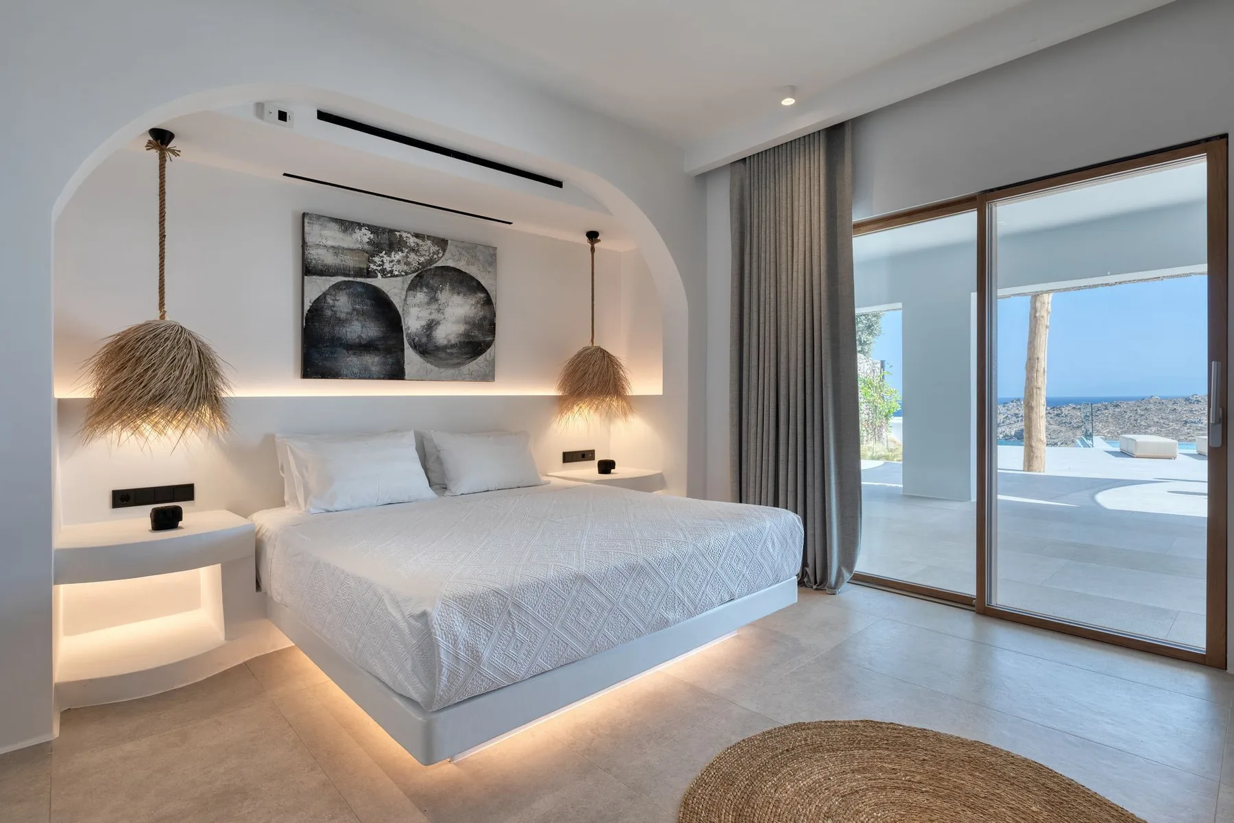 A bright bedroom with a large bed, bedside tables, and sliding glass doors.