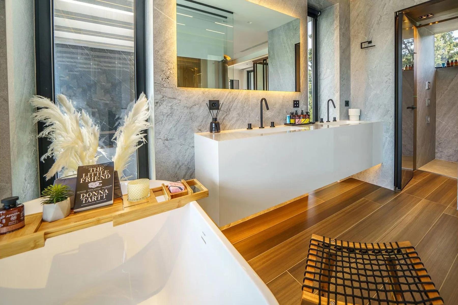 A modern bathroom features a freestanding white bathtub, a floating vanity, a wide mirror, and wood flooring.