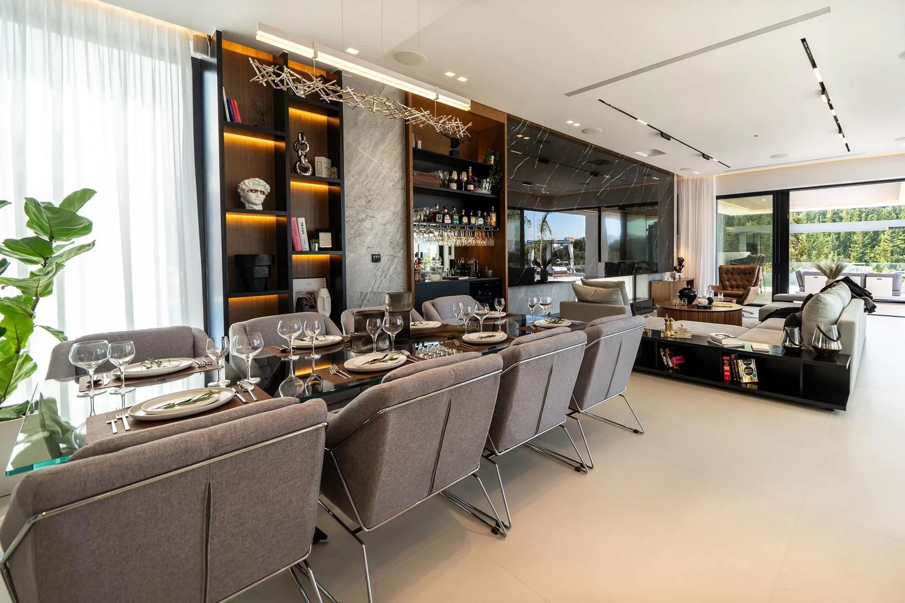 A contemporary dining and living room features a long set dining table, upholstered chairs, and built-in shelving.