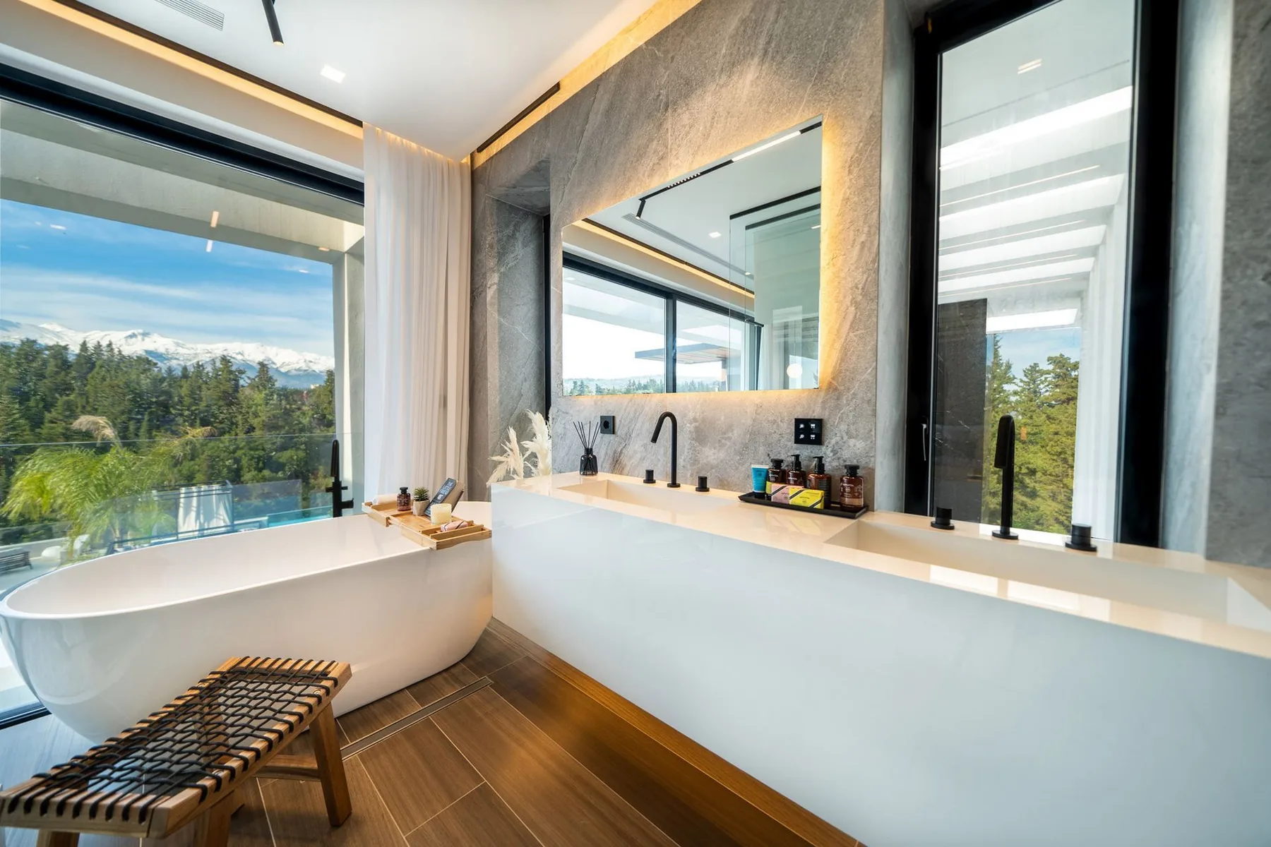 Modern bathroom with a freestanding tub, wood floor, and a long vanity beneath large mirrors.