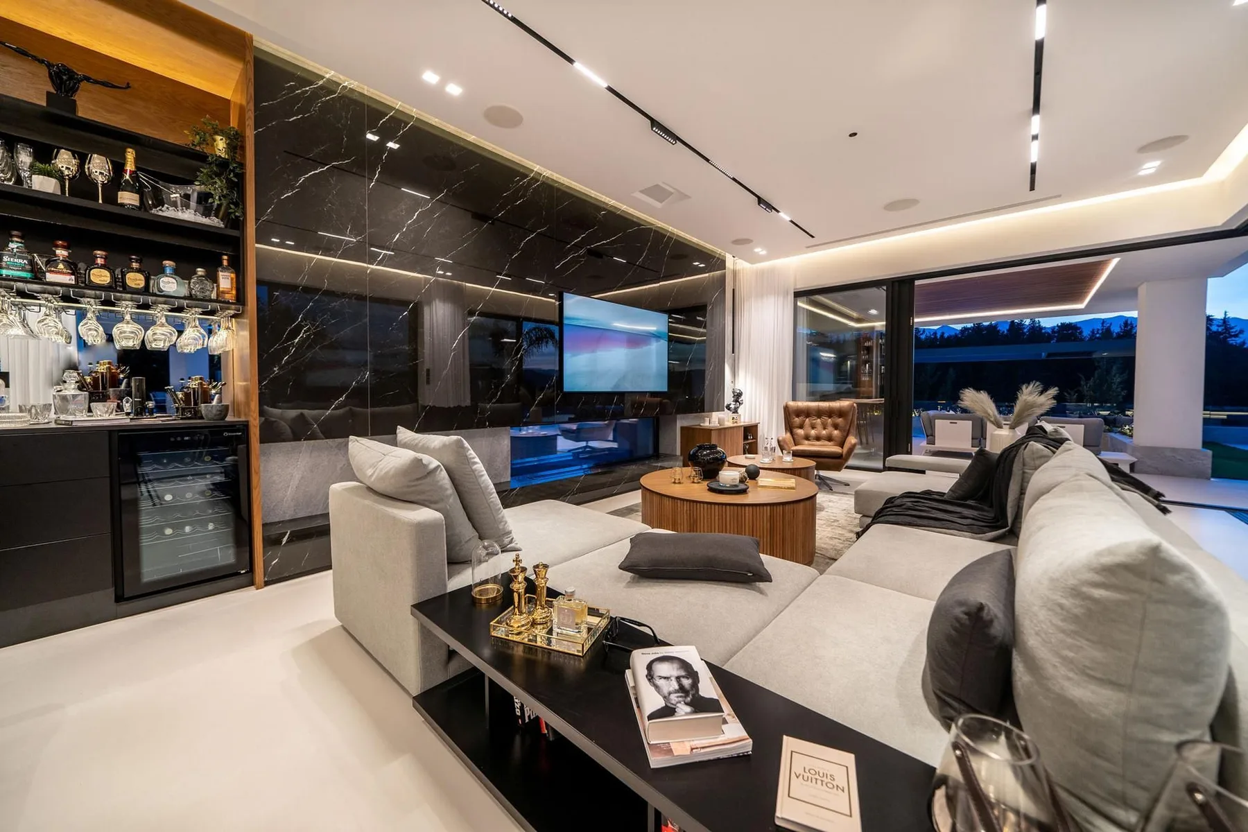 A modern living room features a large sectional sofa, a round coffee table, and a marble TV wall.
