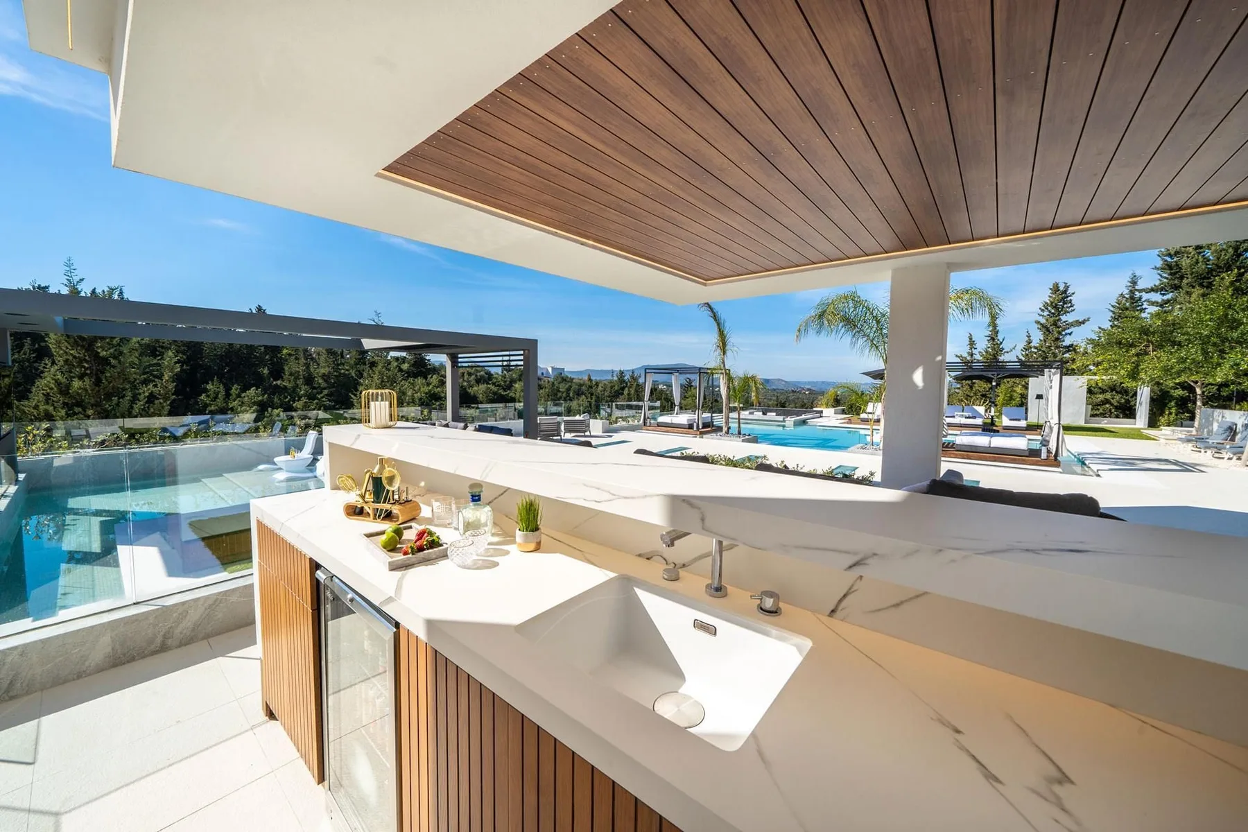 An outdoor kitchen counter with a sink and bar seating overlooks a swimming pool and landscaped terrace.